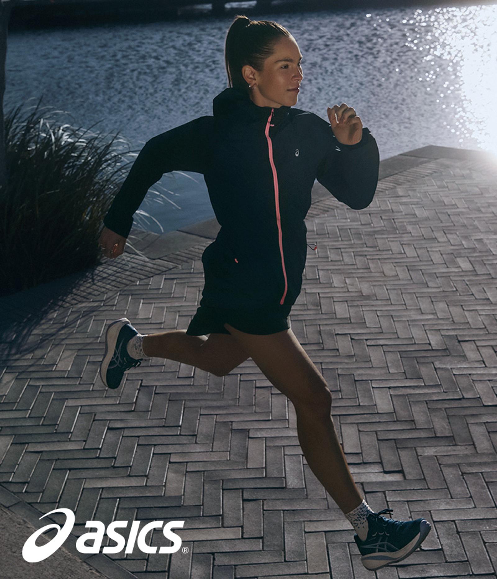 Woman in ASICS gear running on a paved path next to water. ASICS logo visible.