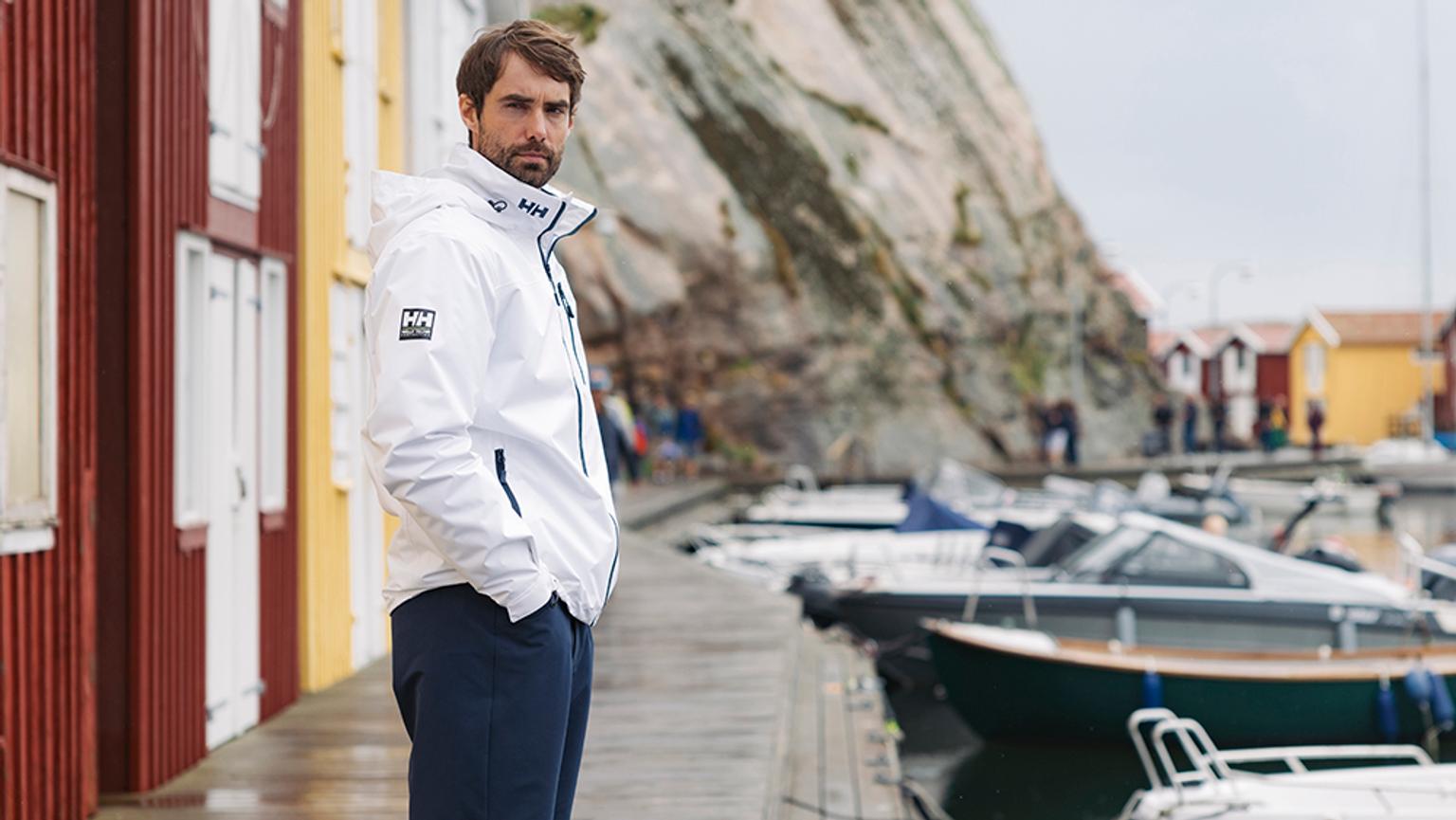 a man in a white jacket is standing on a dock next to boats .