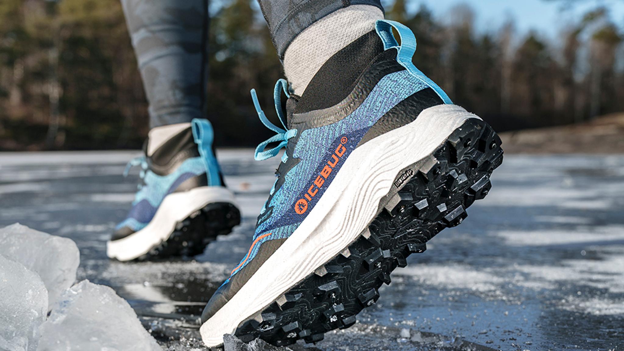 A person wearing blue Icebug winter running shoes with studded soles walks on ice.