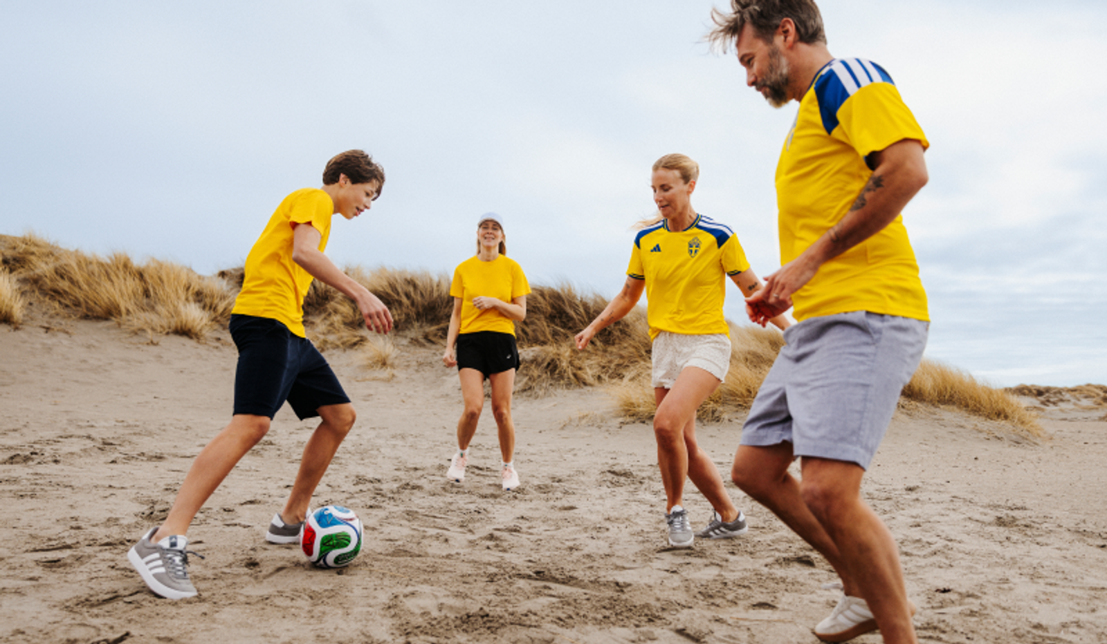 Four people in yellow shirts playing soccer on sand dunes.