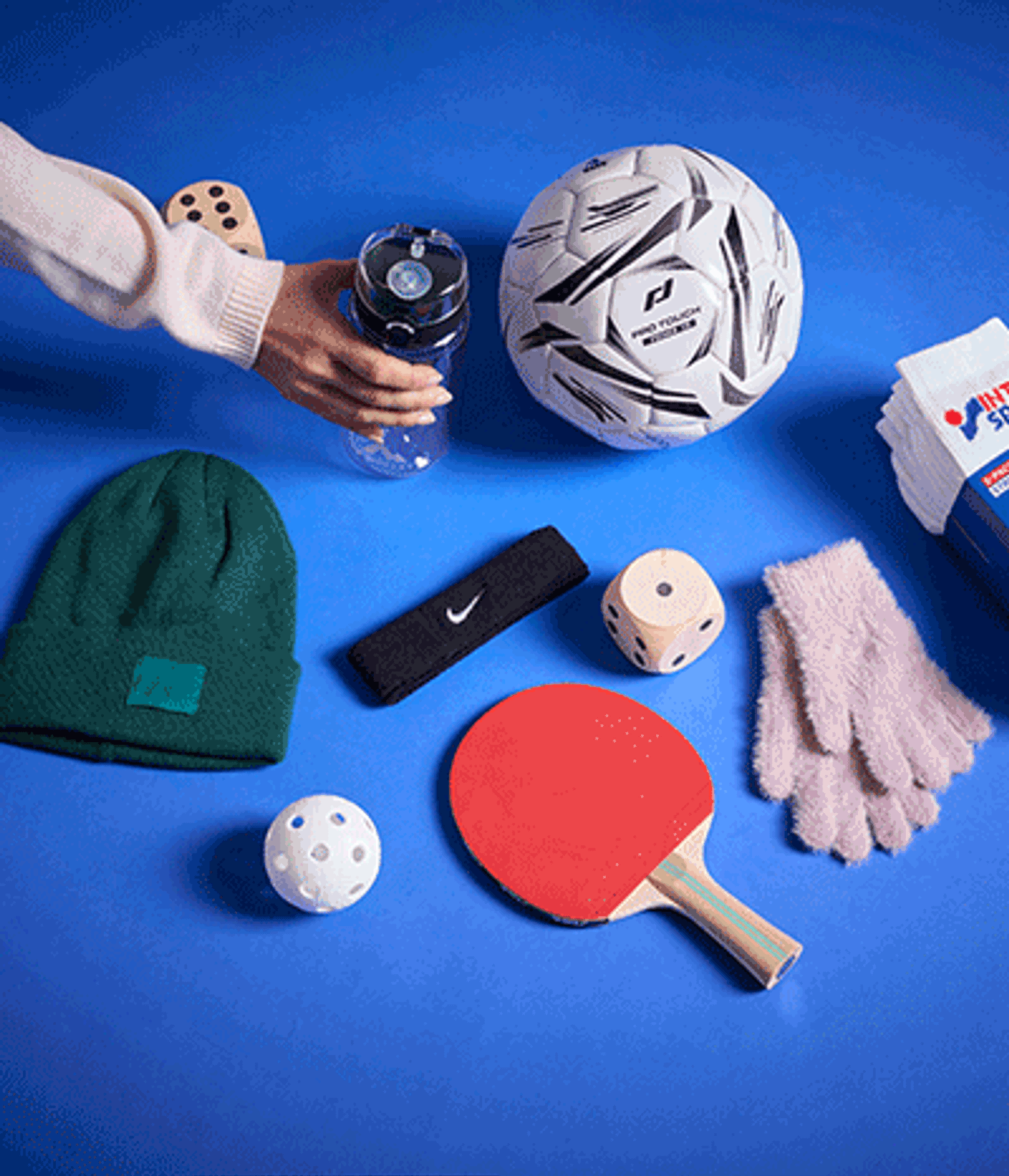 Sports and casual items on a blue background: a soccer ball, water bottle, green beanie, pink gloves, red ping-pong paddle, Nike headband, and white socks.
