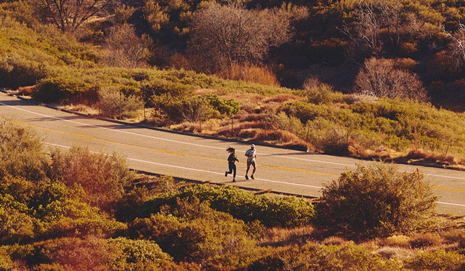 two people are running down a road in the mountains .