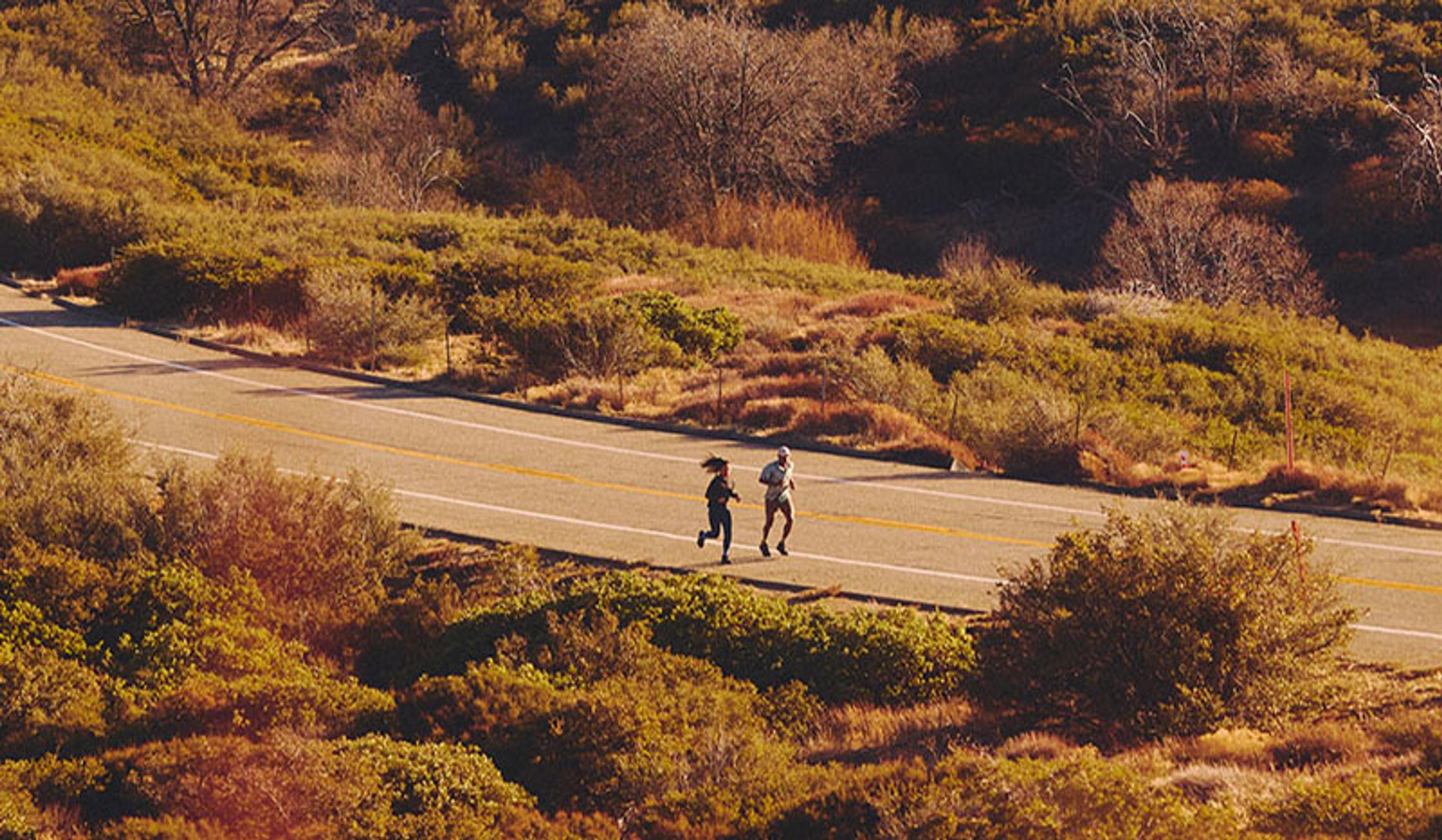 two people are running down a road in the mountains .