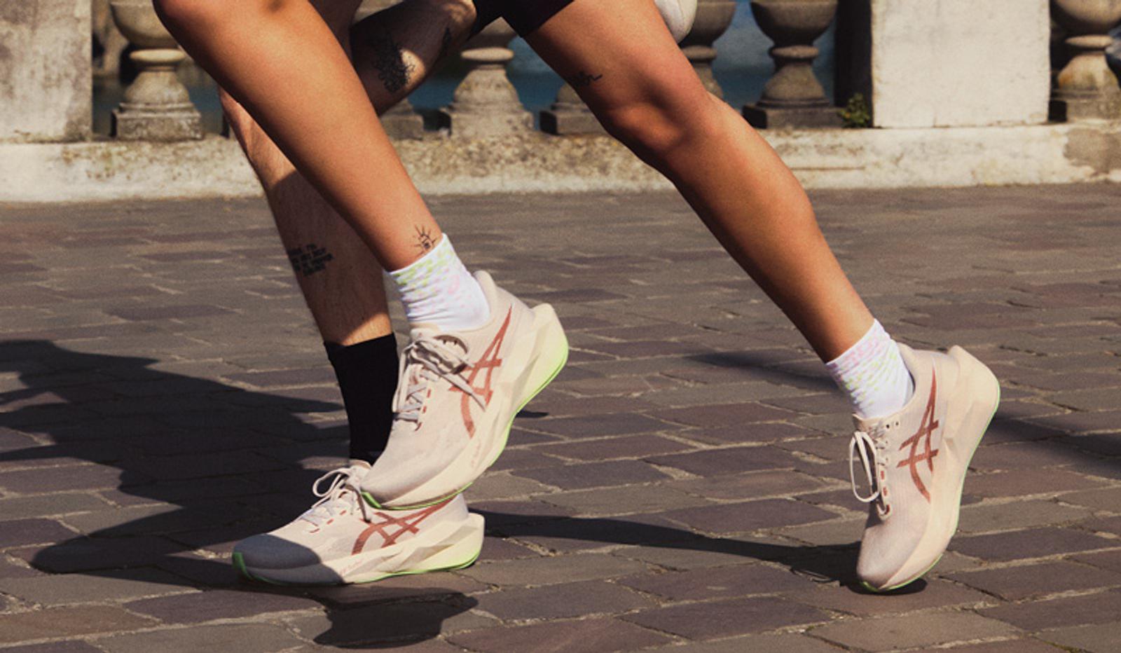 Close-up of two runners' legs wearing beige Asics shoes on a paved surface.