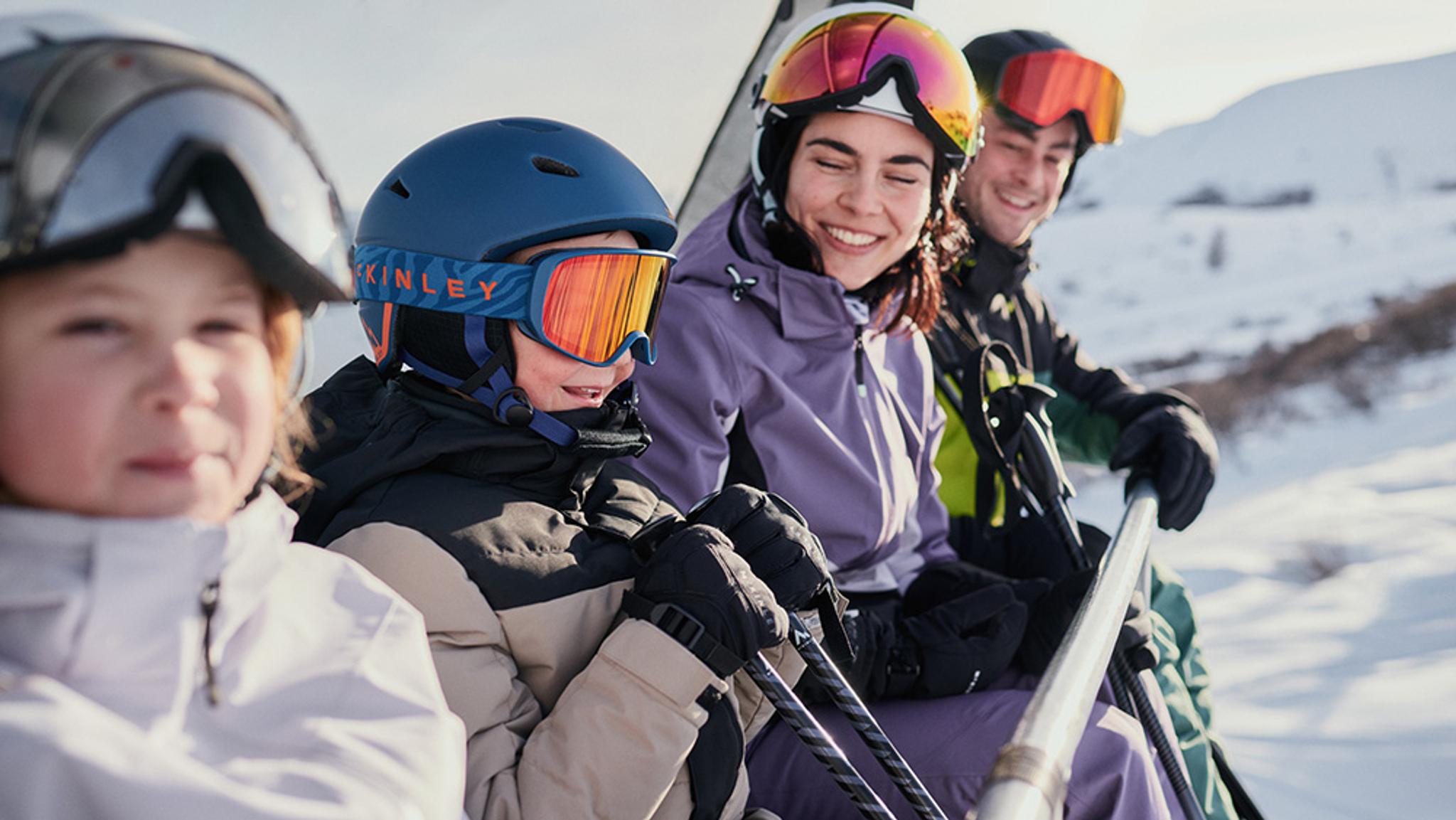 A family of four in ski gear rides a chairlift up a snowy mountain.