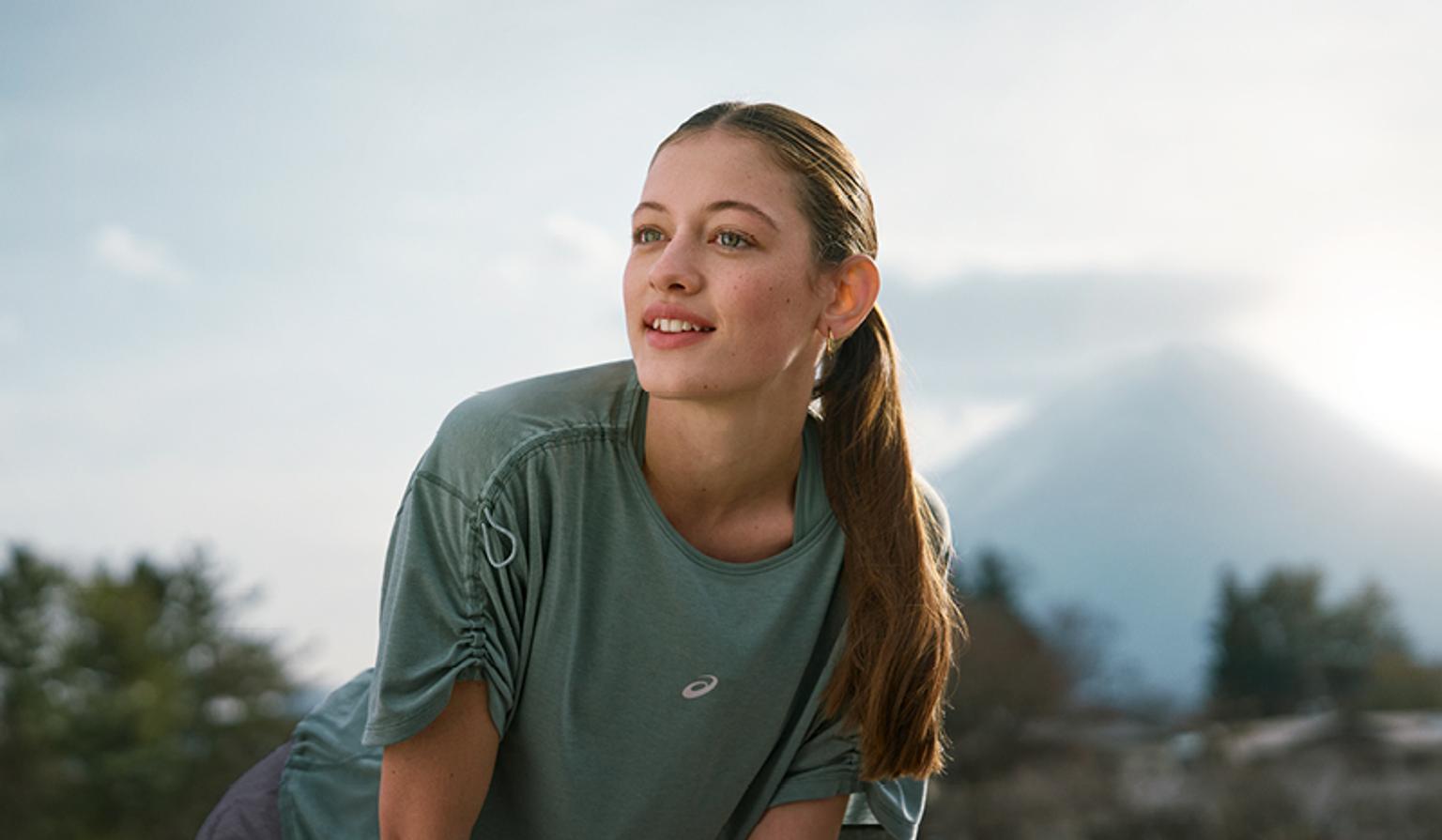 a young woman is stretching her legs in front of a mountain .
