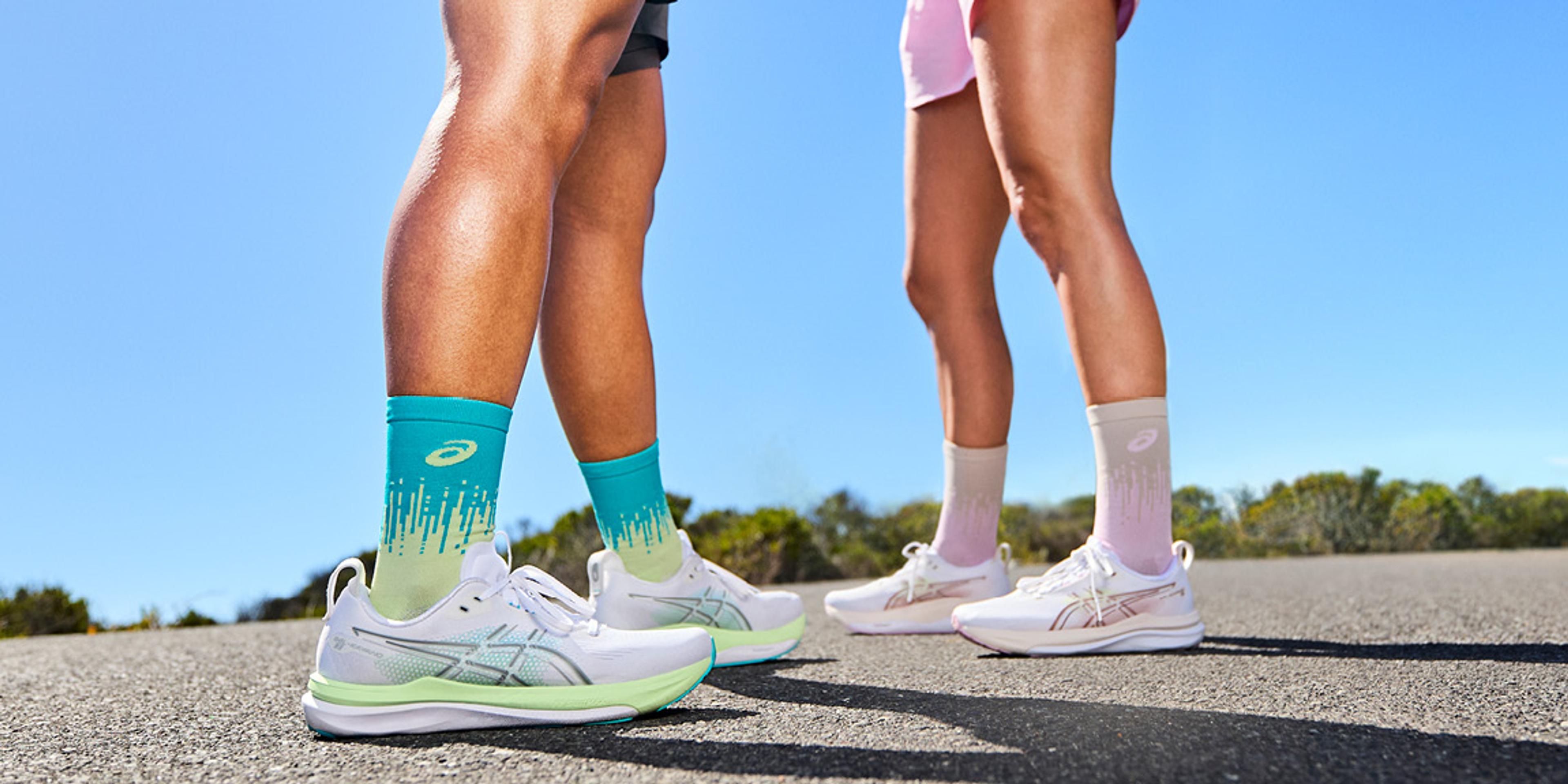 Two pairs of legs wearing ASICS running shoes and colorful gradient socks on an outdoor road.