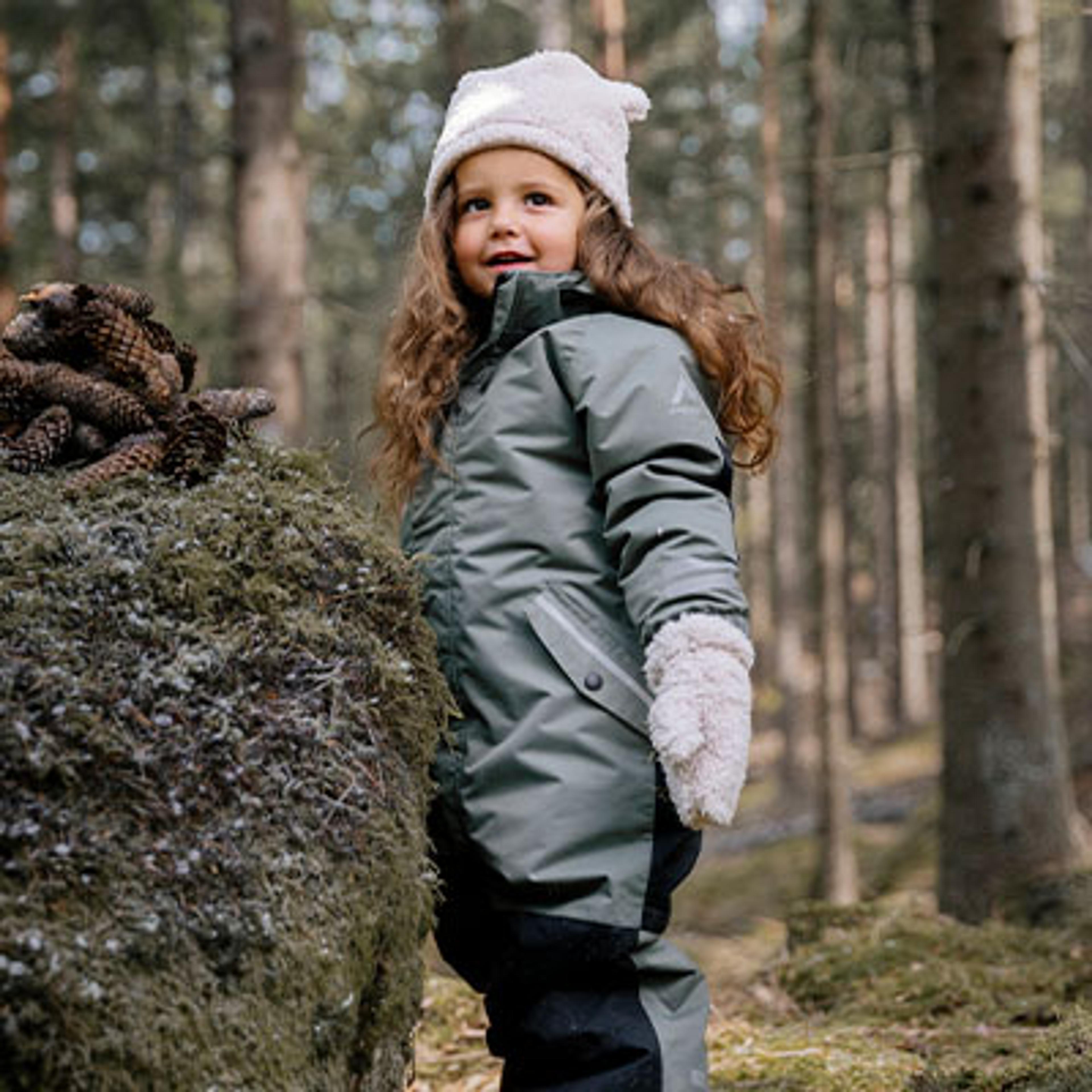 a little girl is standing next to a pile of pine cones in the woods .