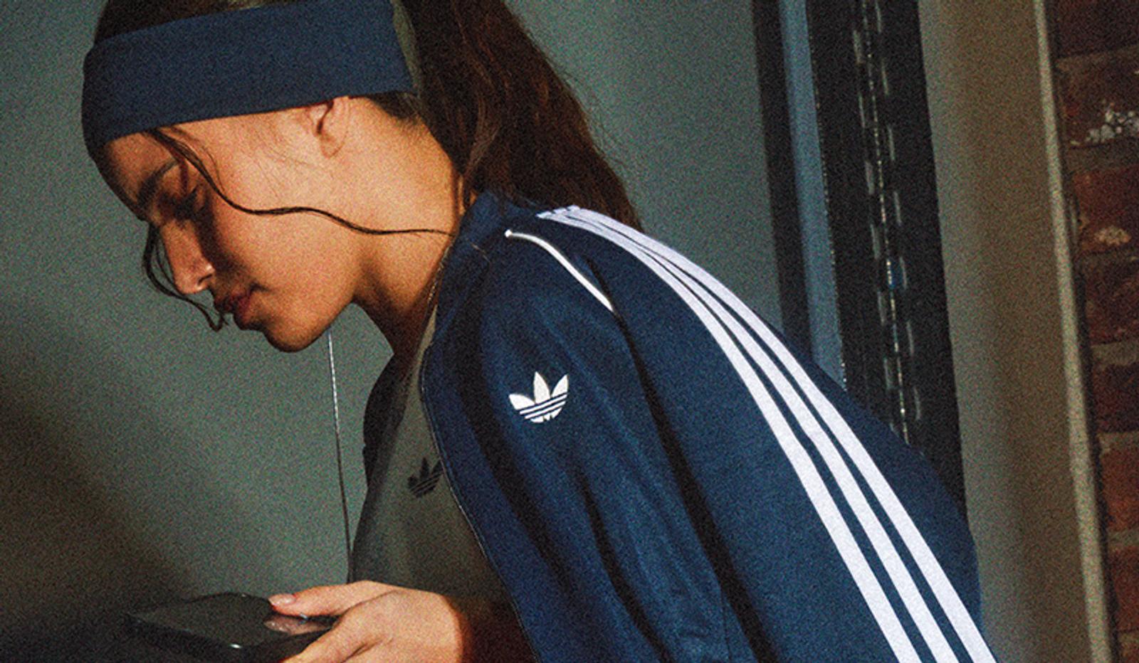 Woman in a navy Adidas track jacket and headband looking at a smartphone.