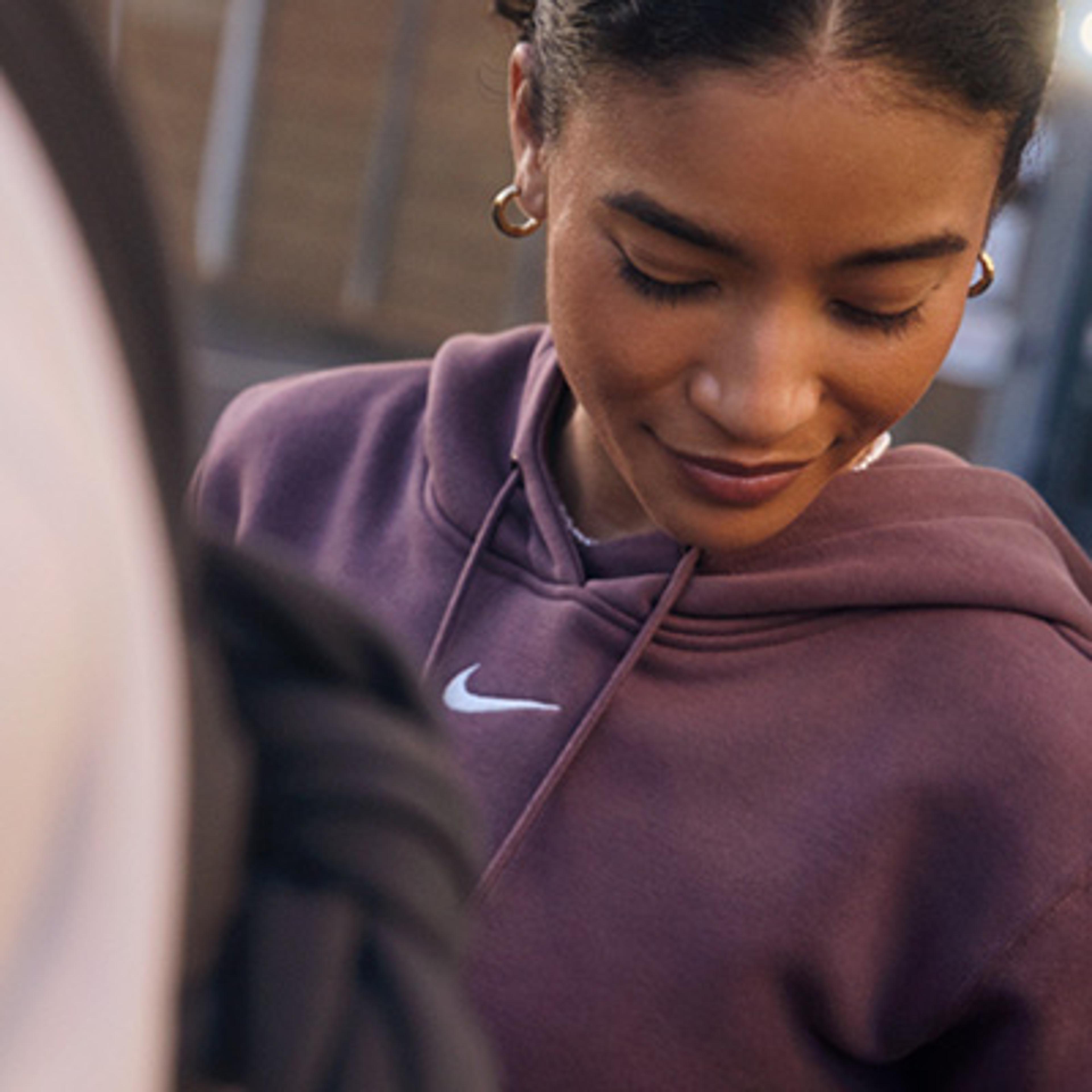 Woman in a plum Nike hoodie looking down with a slight smile.