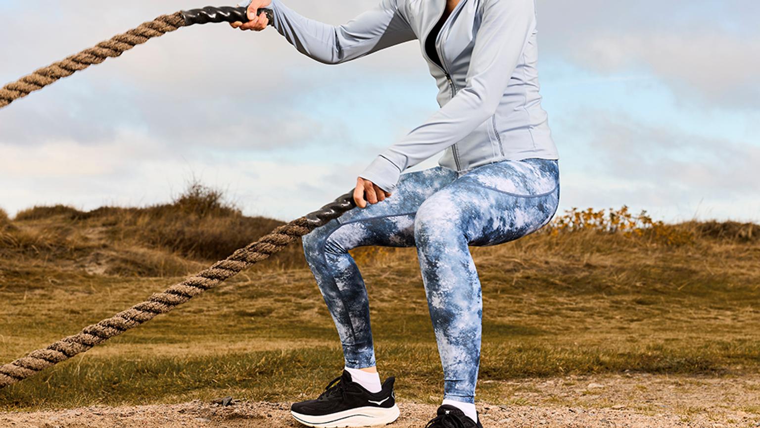 Person squatting while pulling a thick rope outdoors in new nice tights.