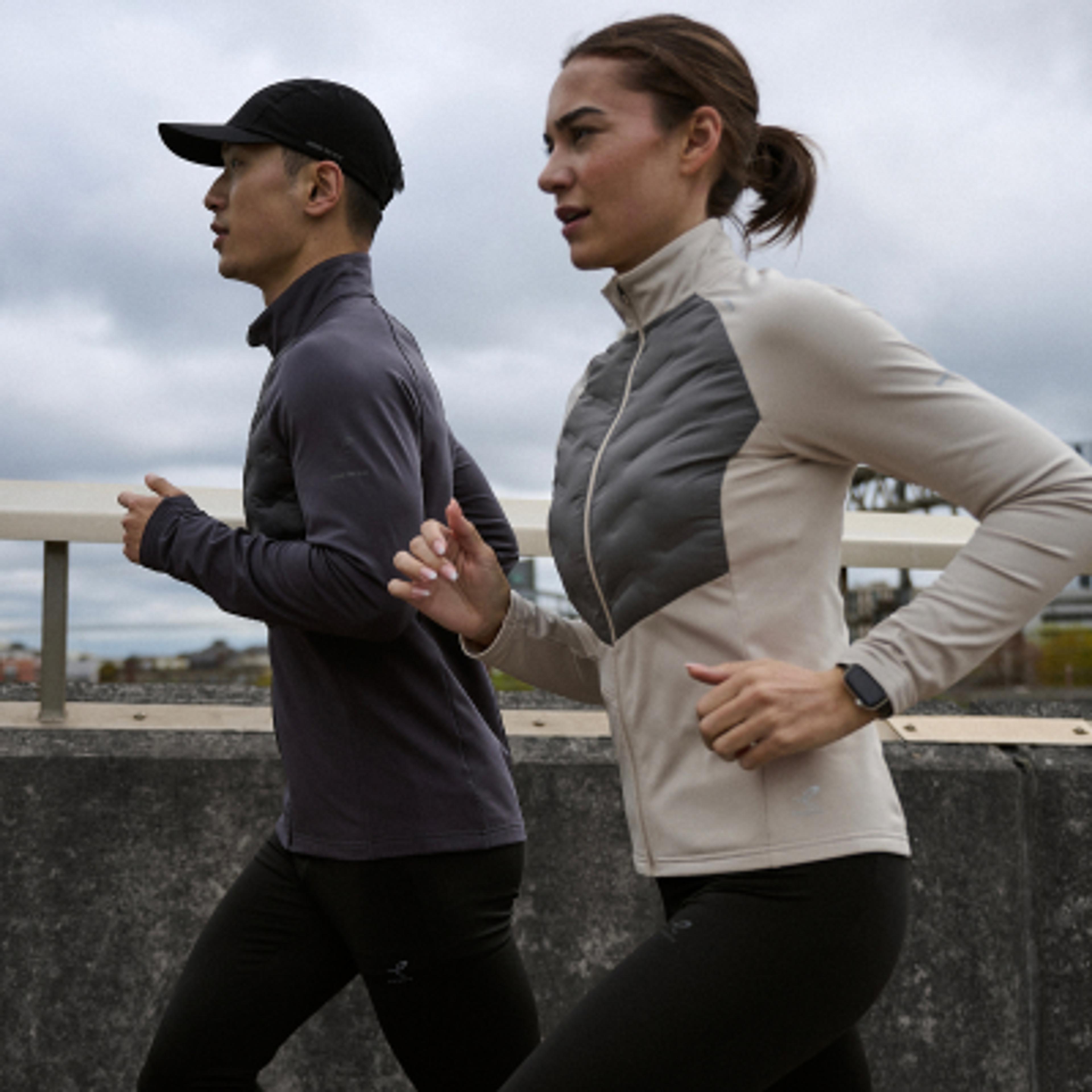 A man and woman running outdoors in athletic jackets.