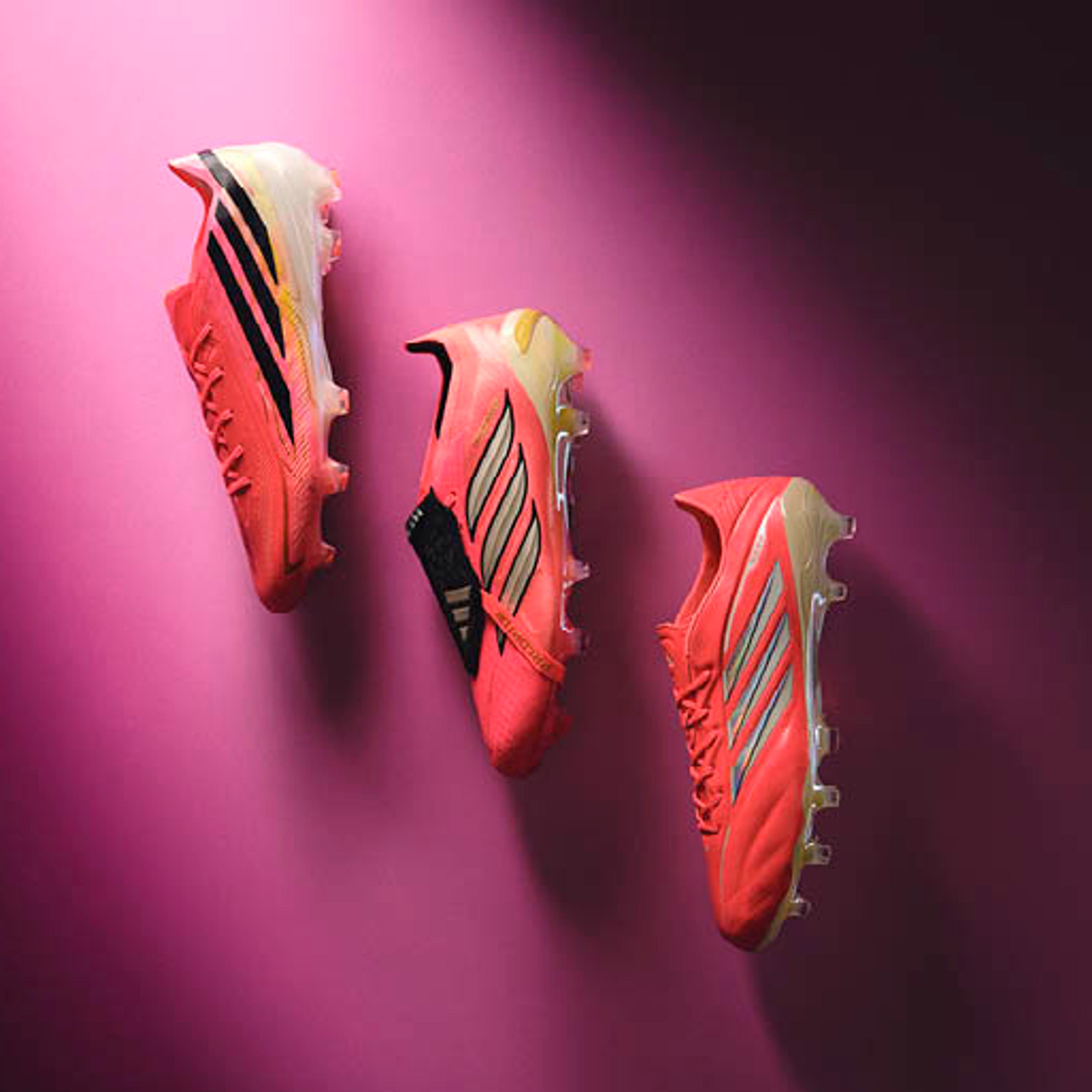 Three coral-pink Adidas football boots on a pink background.