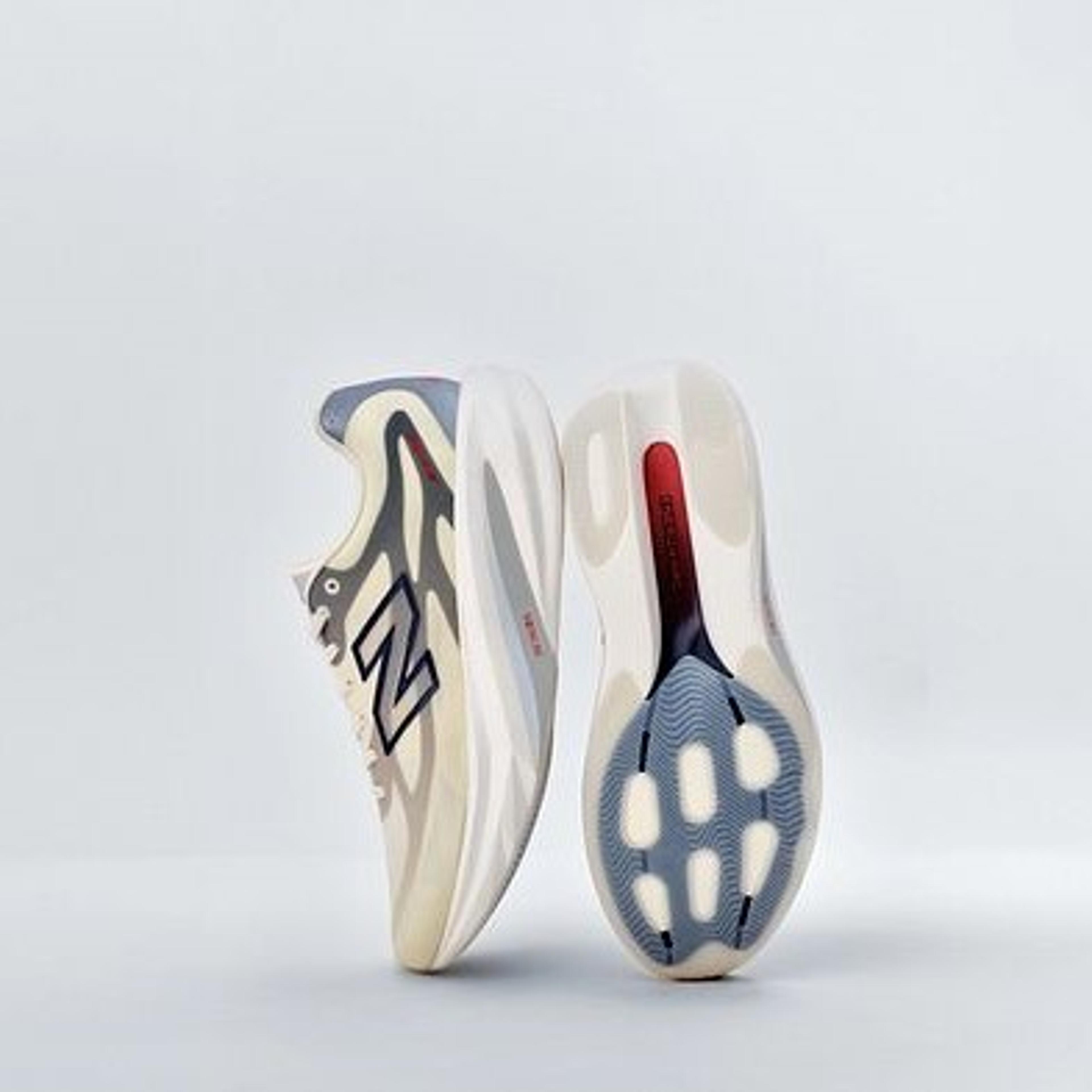 A pair of New Balance sneakers, one showing its cream and grey patterned upper, the other its sole with blue and red accents.