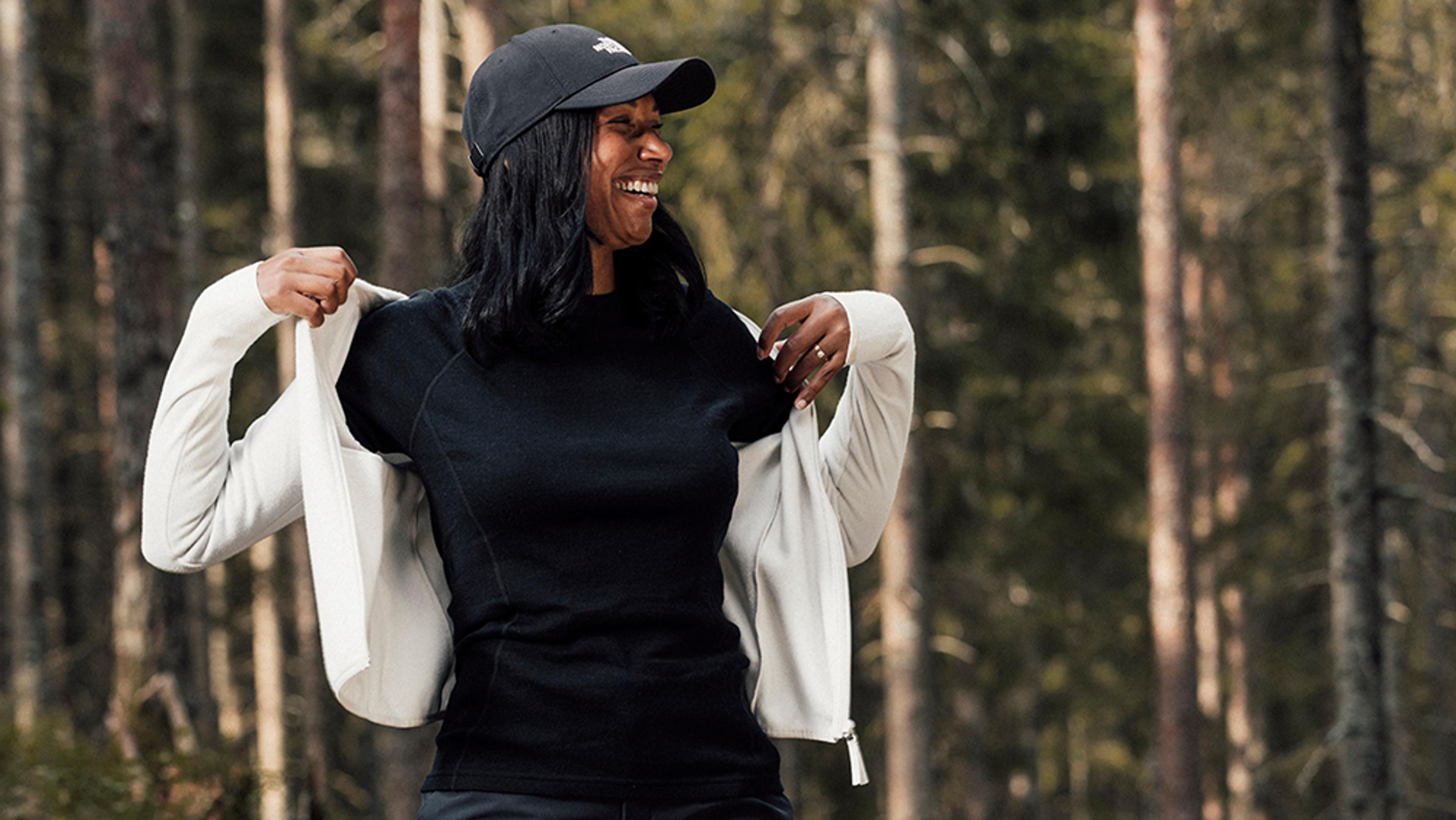 a woman wearing a black hat and a white jacket is standing in the woods .