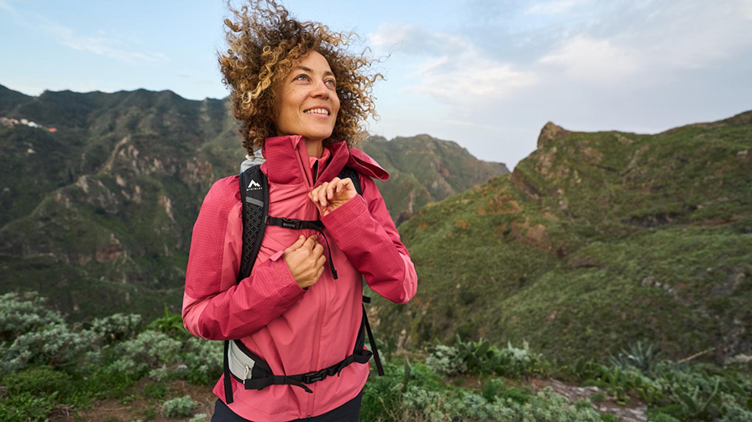 a woman with a backpack is standing on top of a mountain .