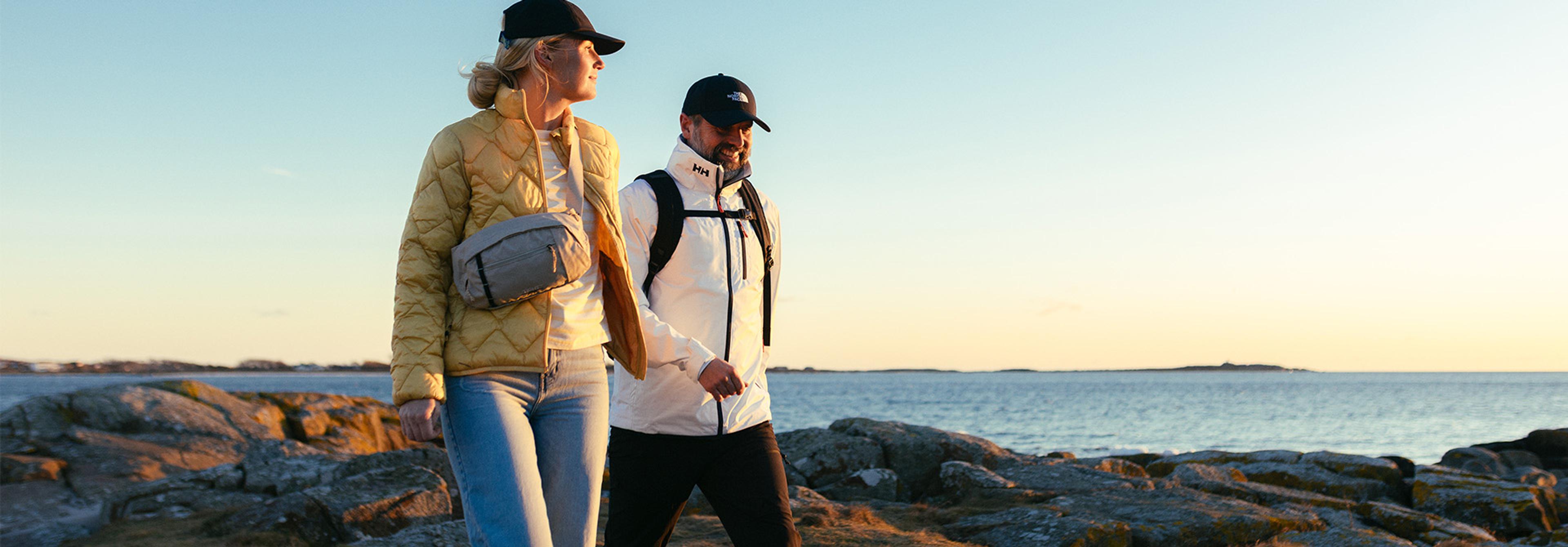 A couple walking along a rocky coastline by the ocean at sunset.