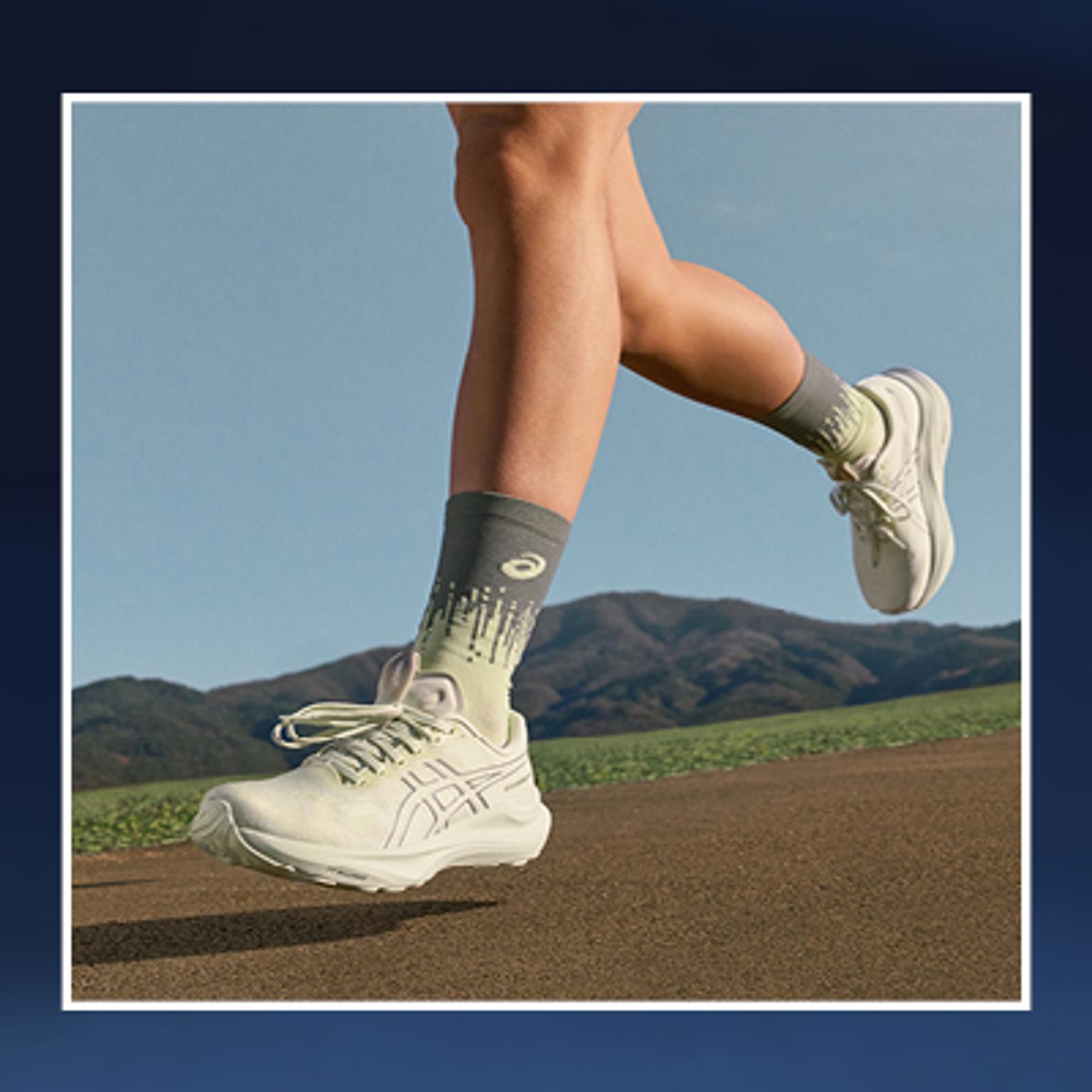 a person wearing white asics shoes and socks is running on a dirt road .