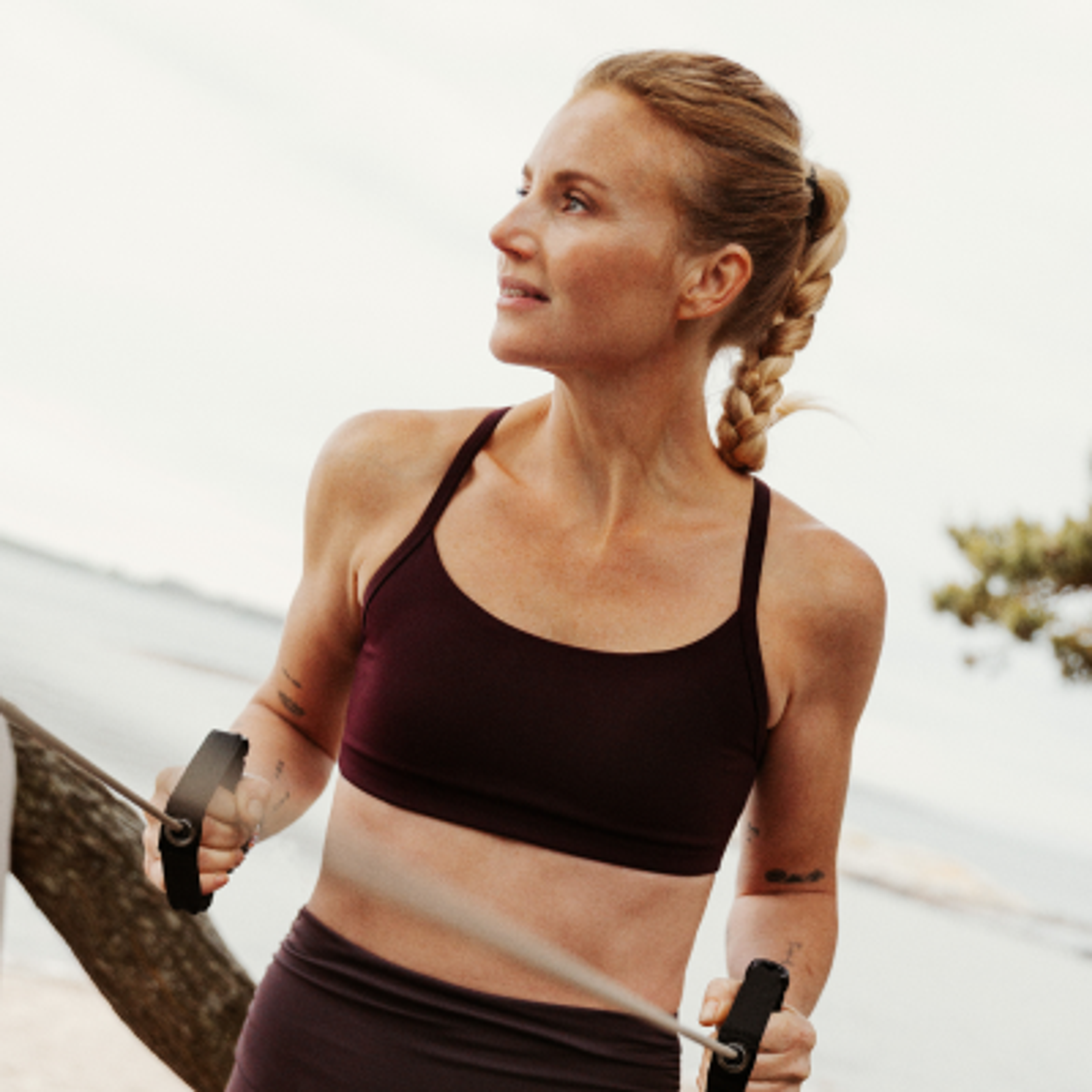 A woman with braided hair exercises outdoors with a resistance band.