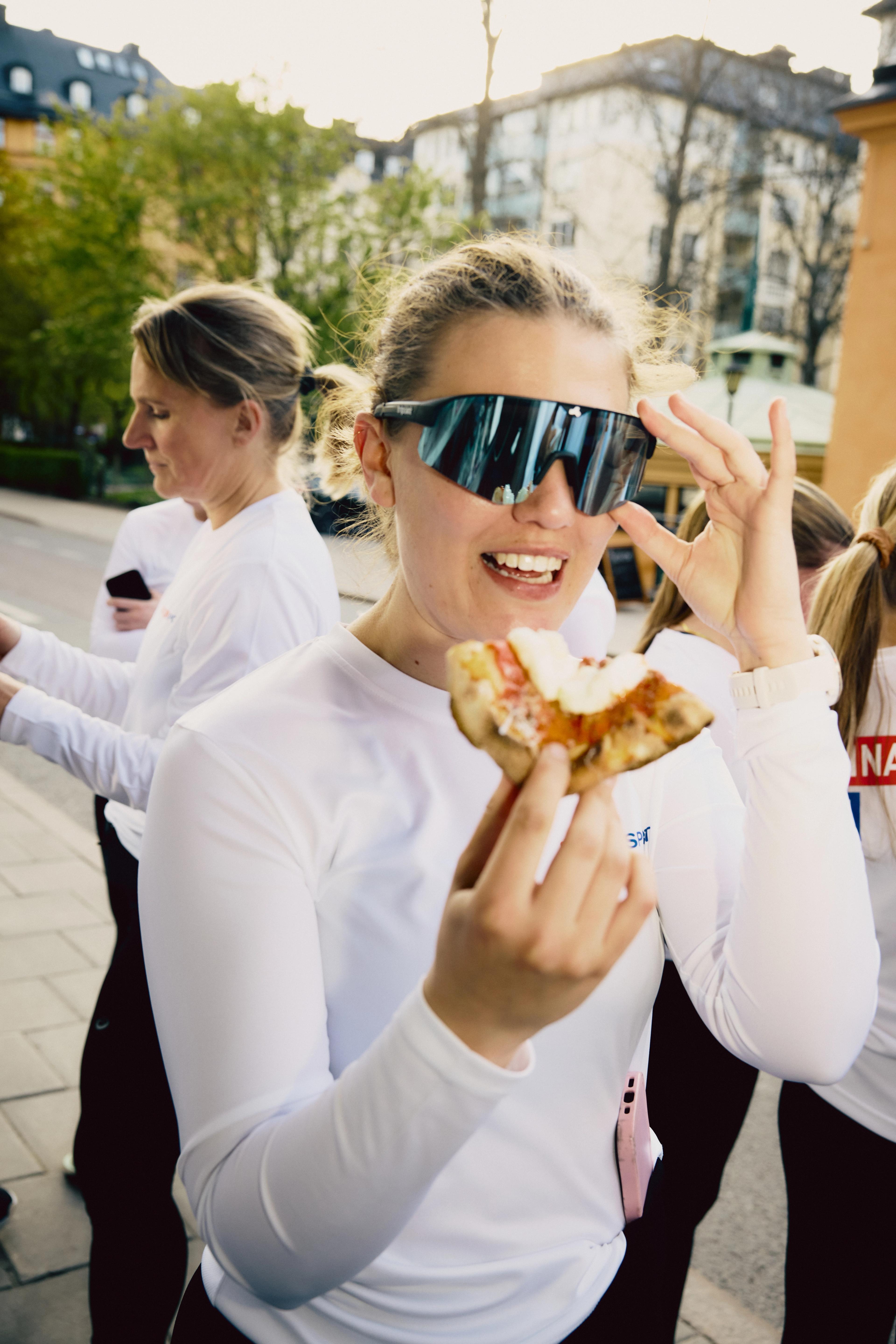 a woman wearing sunglasses is eating a slice of pizza