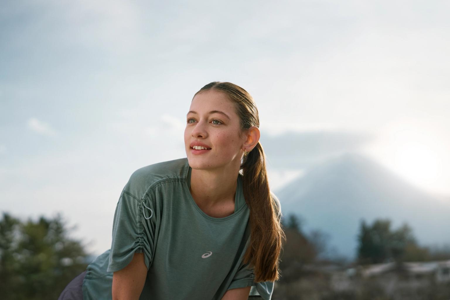 a woman in a green shirt is standing in front of a mountain .
