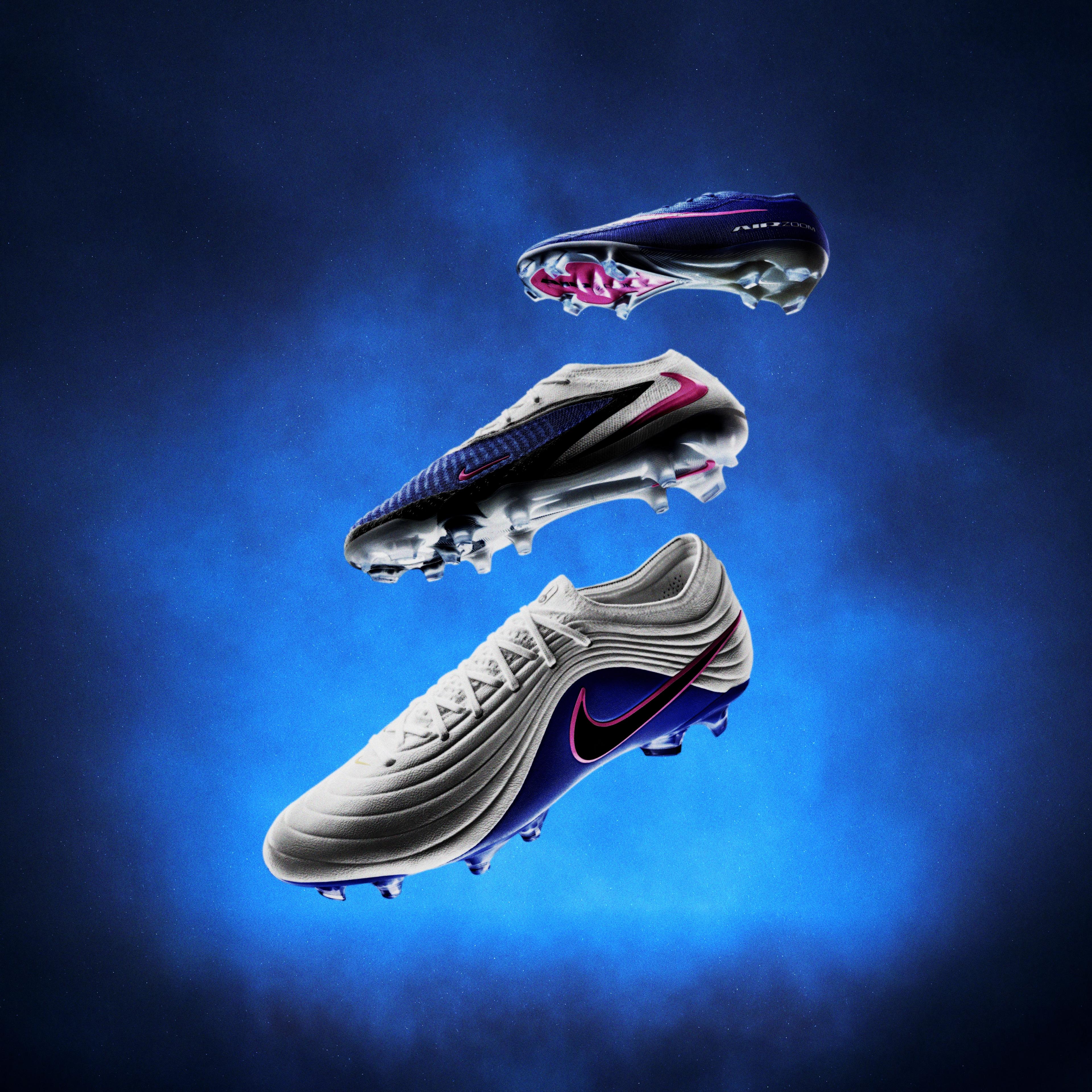 Three Nike soccer cleats in white, gray, and dark blue, with vibrant accents, floating against a smoky blue background.