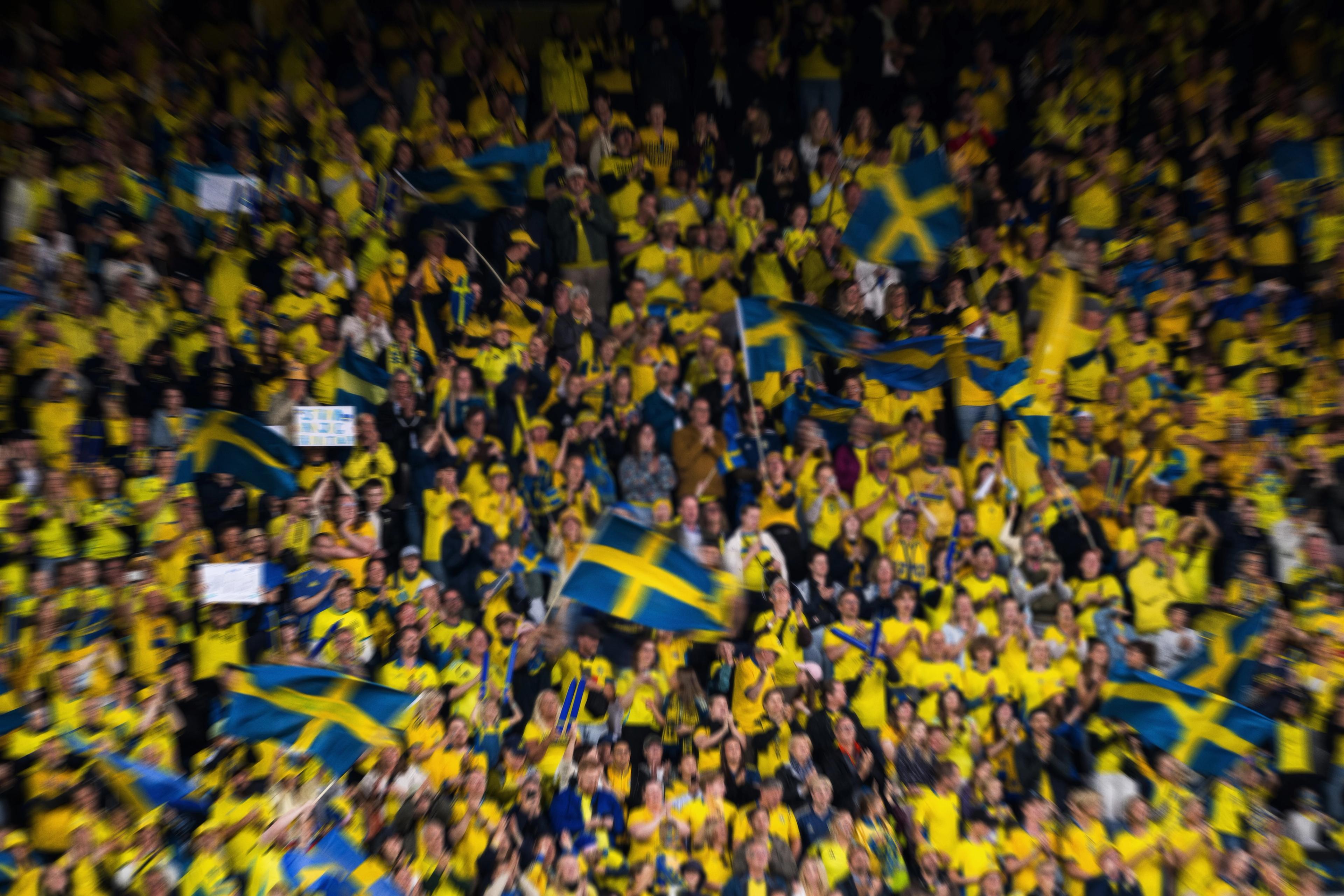 A blurry crowd of people wearing yellow and waving Swedish flags.