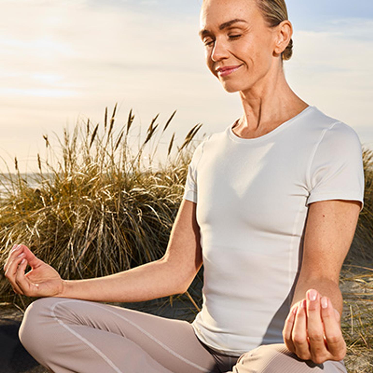 Woman meditating peacefully on a beach.