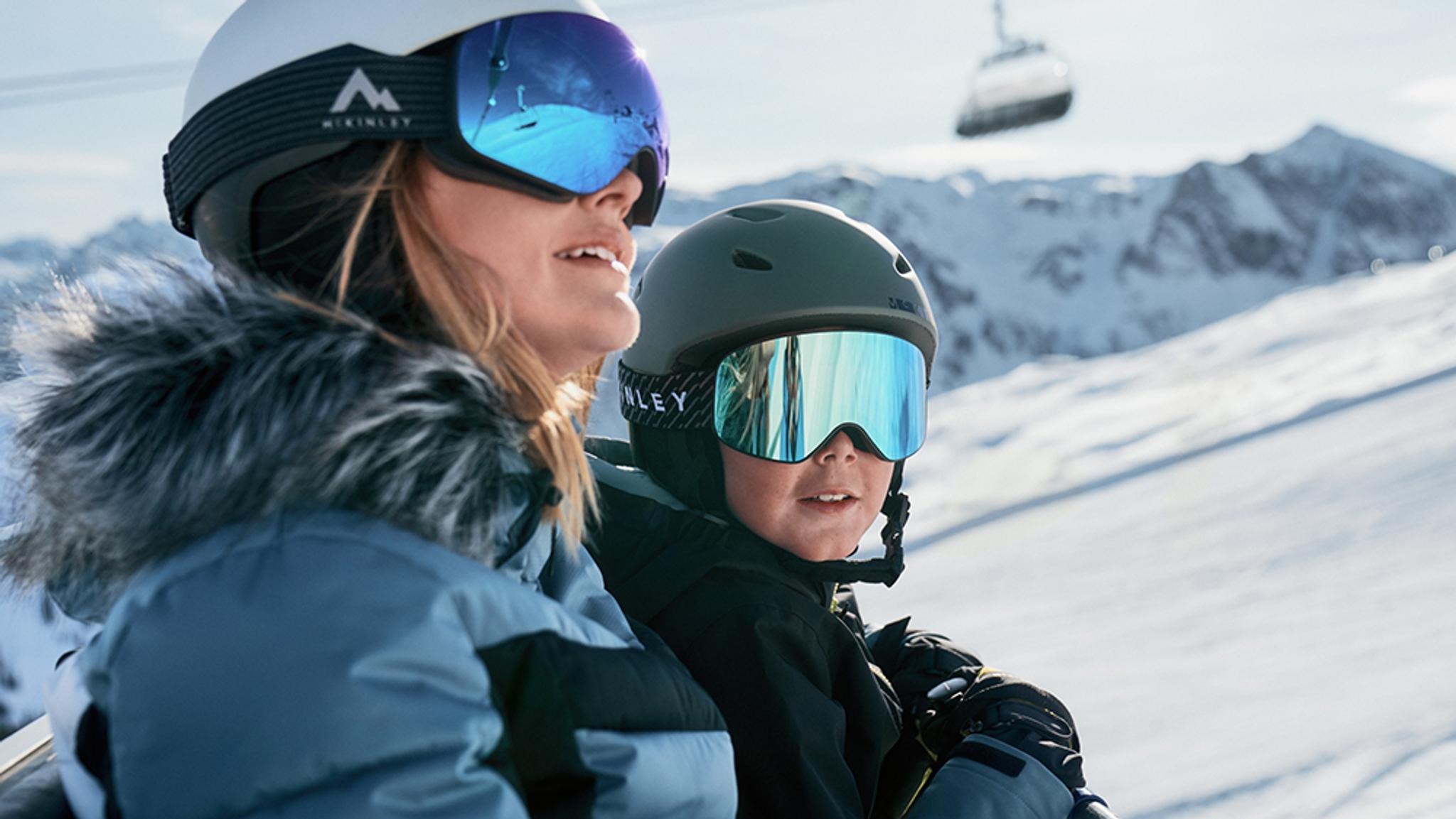 a woman and a child wearing goggles and helmets are sitting on top of a snow covered mountain .