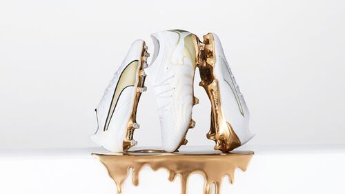 Three white soccer cleats with gold accents, set above dripping metallic gold.
