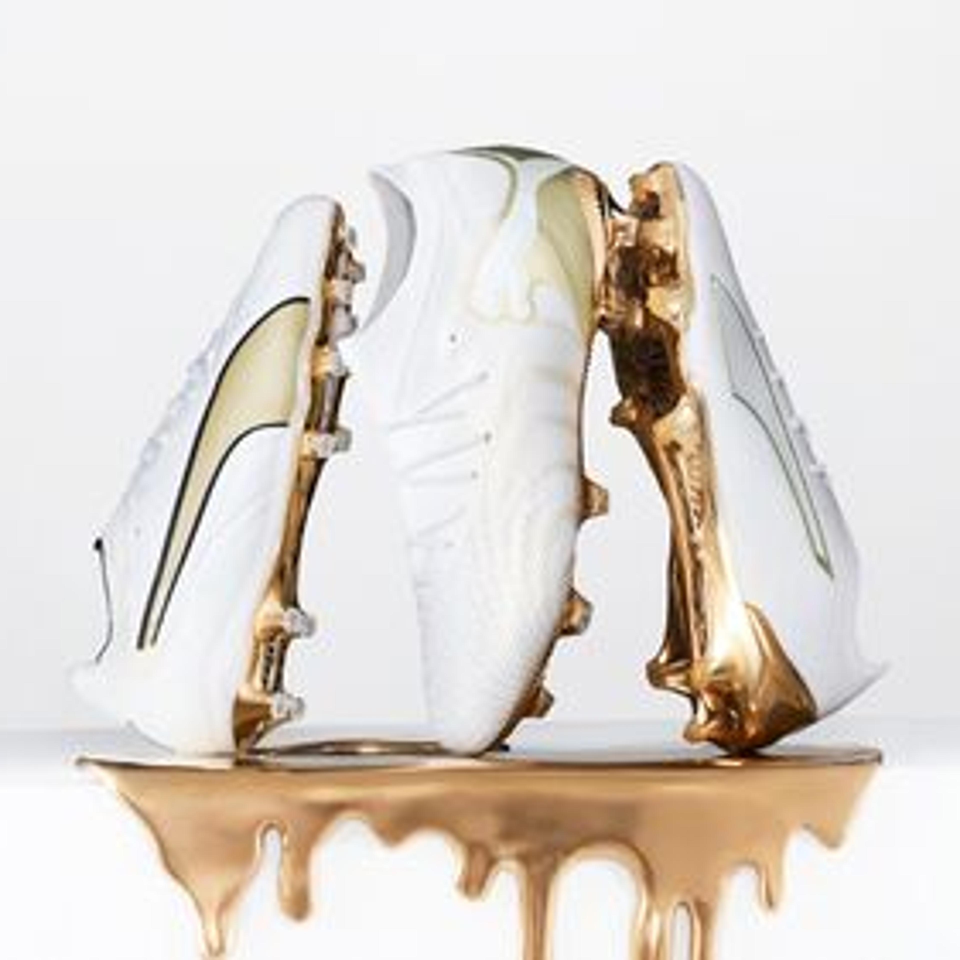 Three white soccer cleats with gold accents, set above dripping metallic gold.