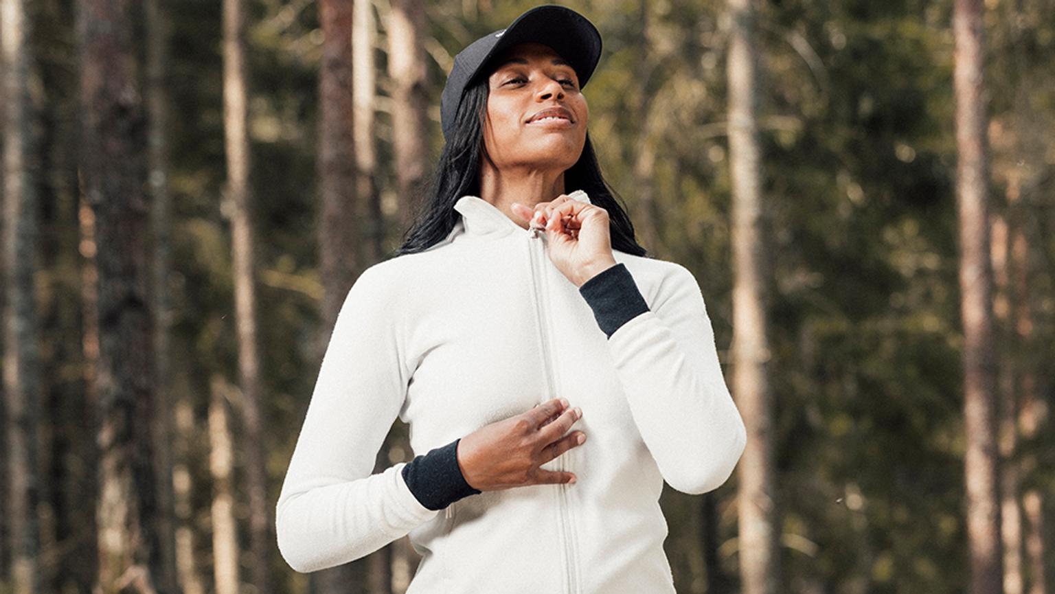 a woman in a white jacket and black hat is standing in the woods .