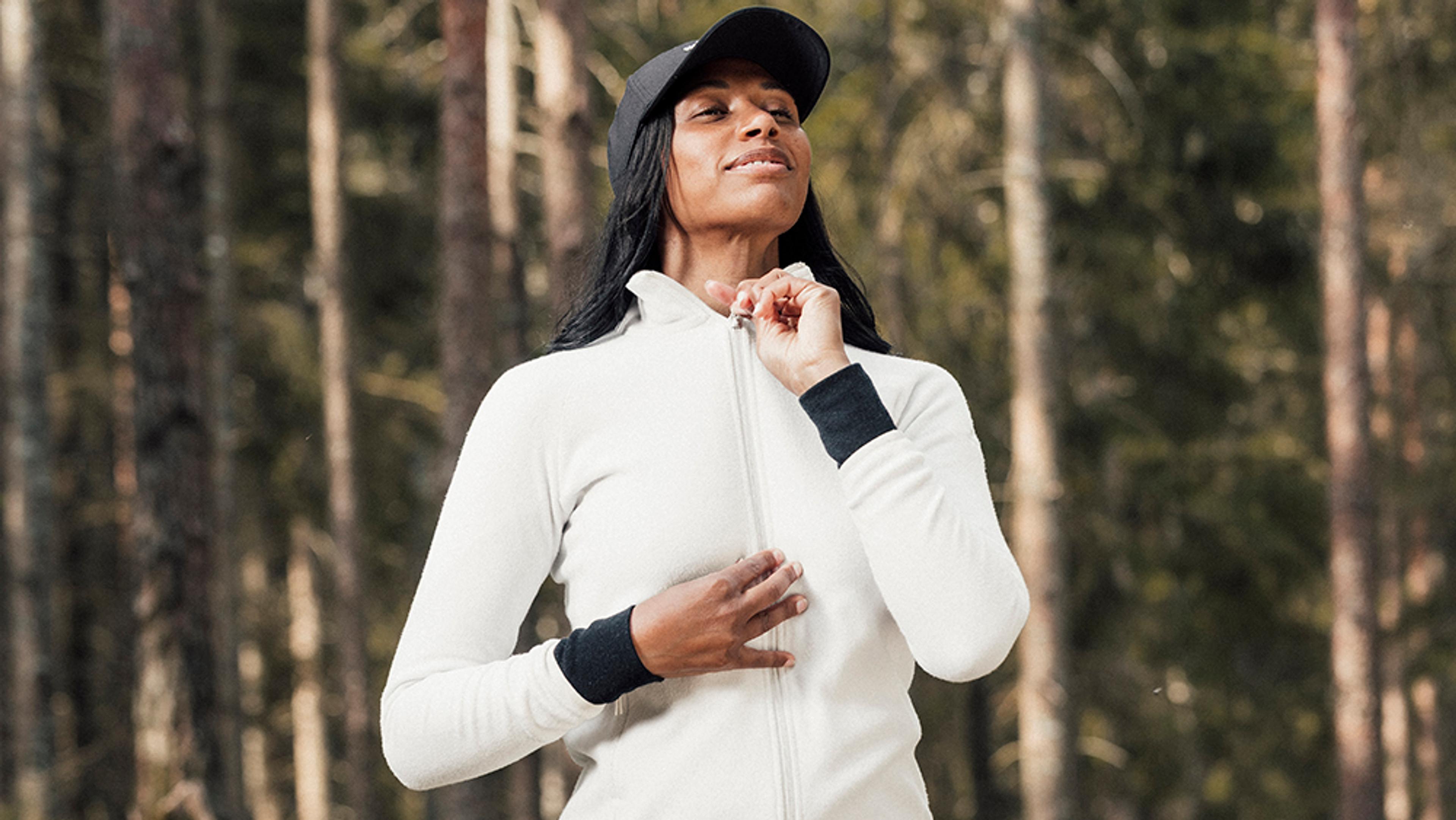 a woman in a white jacket and black hat is standing in the woods .