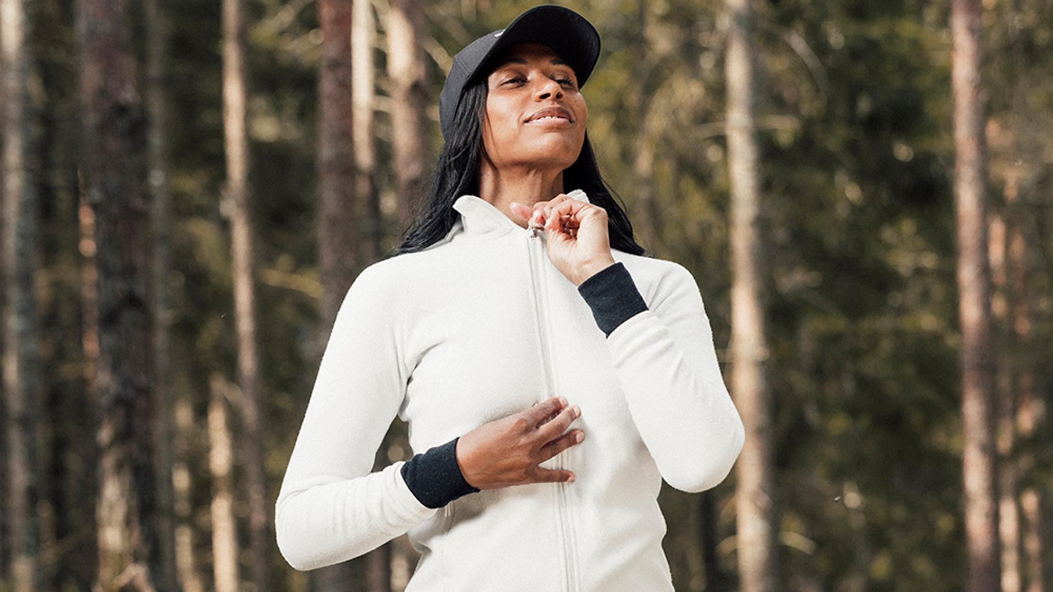 a woman in a white jacket and black hat is standing in the woods .