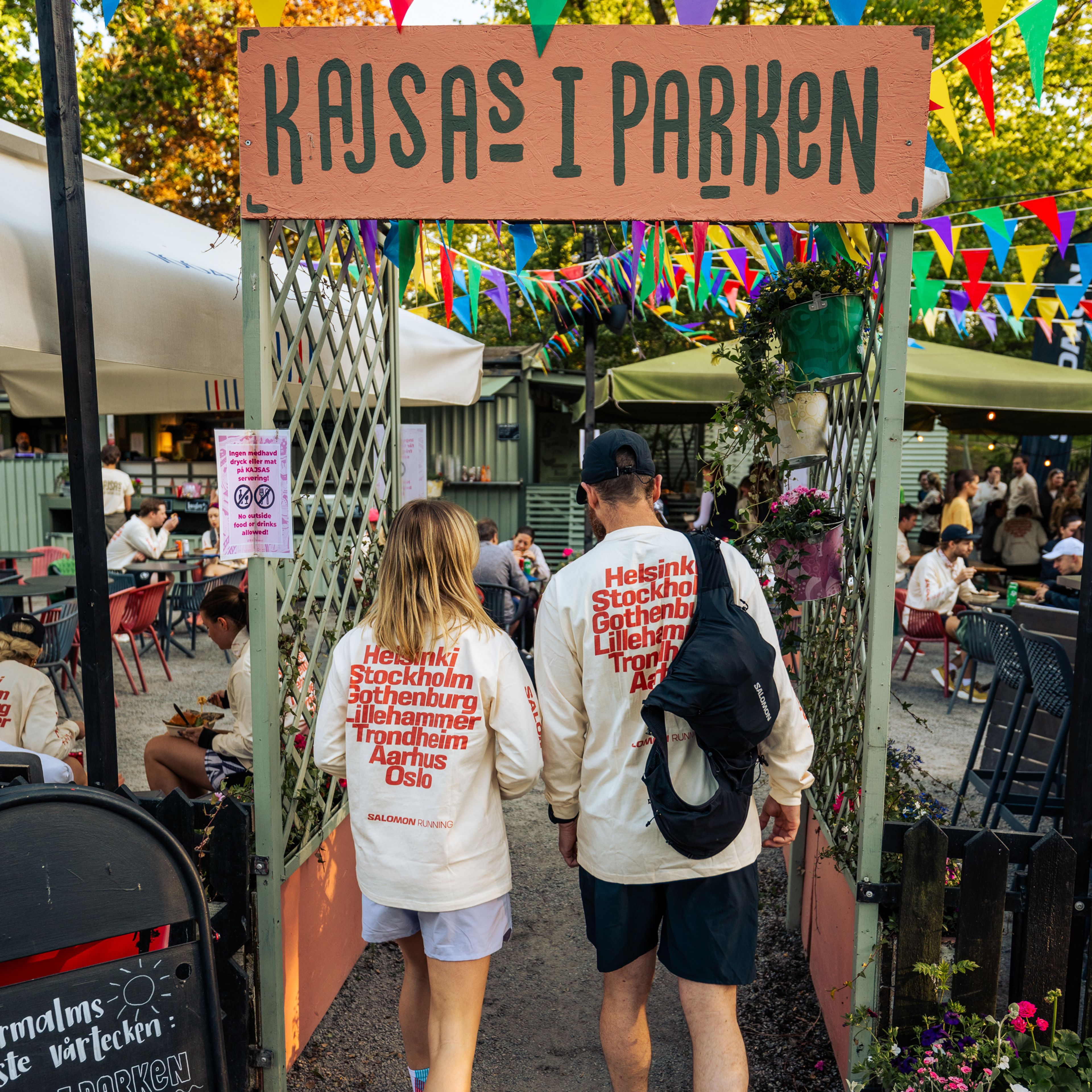 a man and a woman are walking through a gate that says kajsas i parken