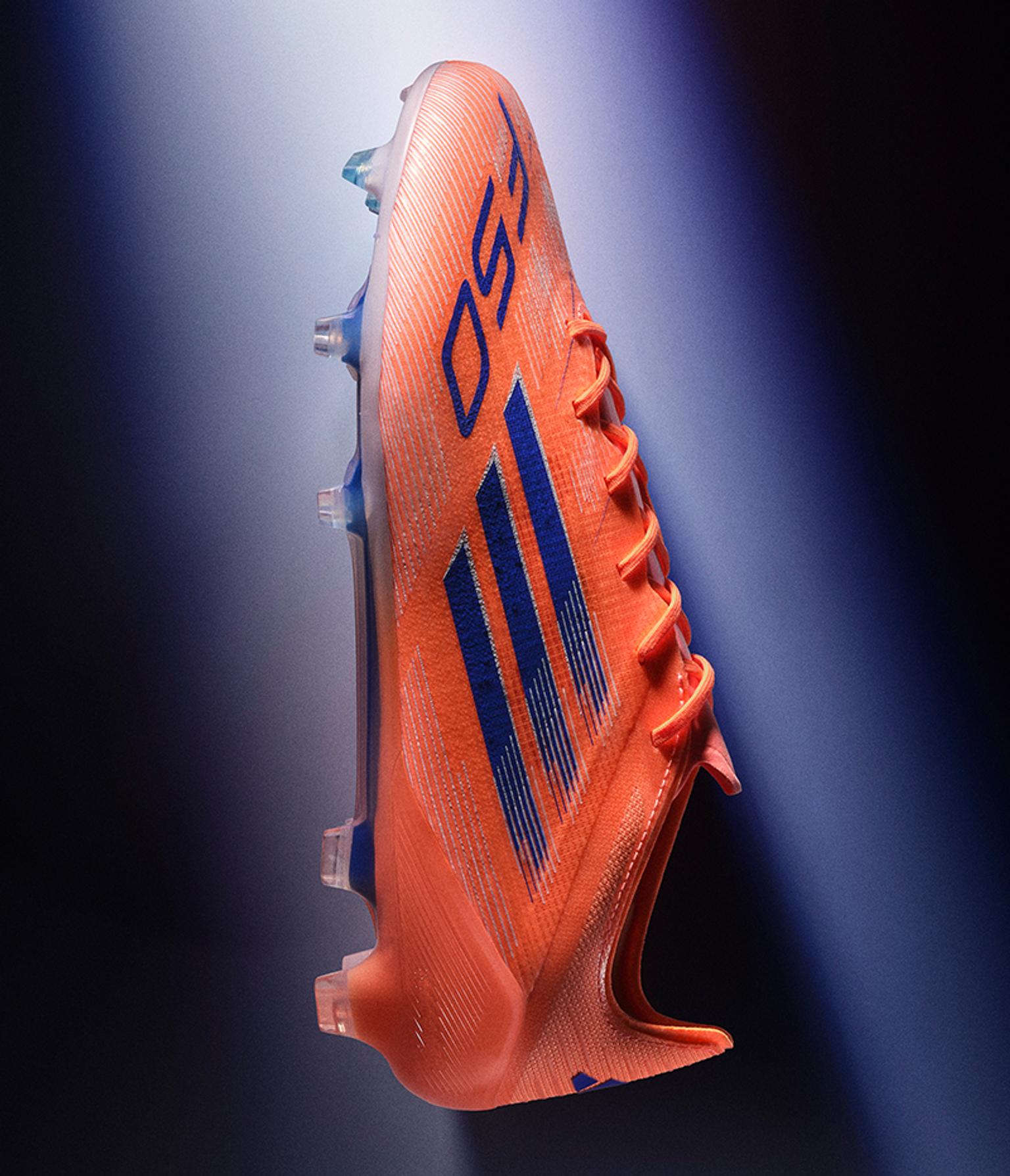 a pair of orange and blue adidas soccer cleats on a blue background .