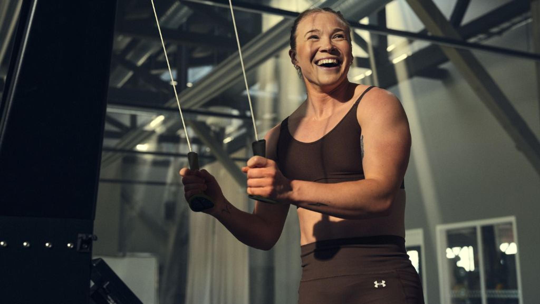 Smiling woman, Jonna Sundling, exercising on a cable machine in a gym.
