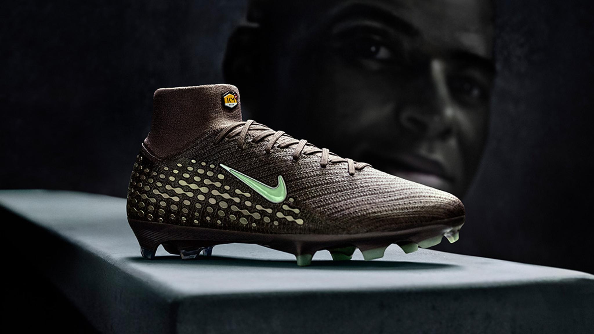 Dark bronze high-top Nike soccer cleat with light green swoosh, sole, and side pattern, in front of a blurred dark face.