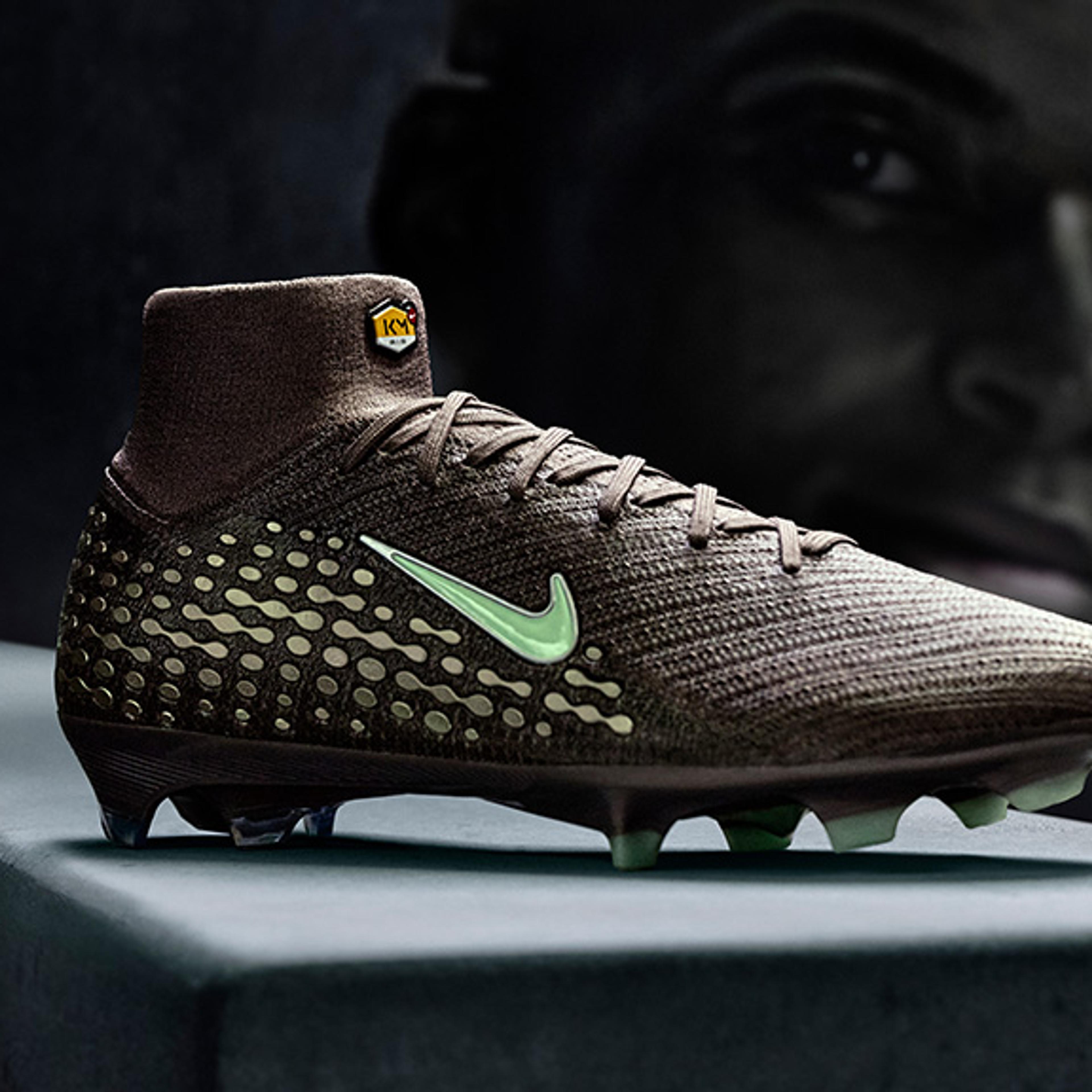 Dark brown Nike soccer cleat with light green swoosh, dotted pattern, and studs, featuring a high collar with a TN logo, against a dark silhouetted face.