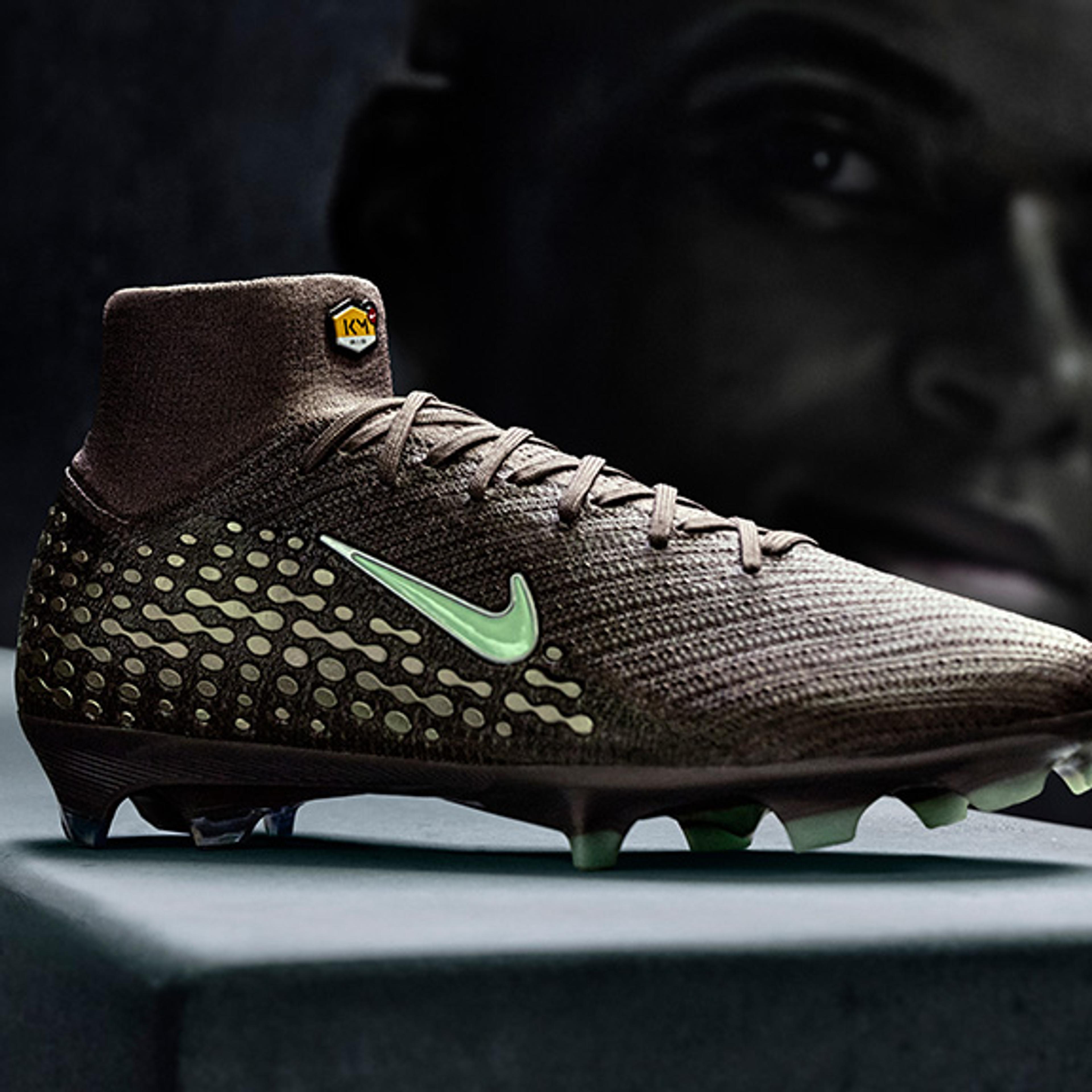 Dark brown football boot with a light green Nike swoosh, studded sole, and ankle collar, in front of a dark, blurry face.
