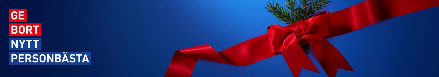 Red ribbon bow with a pine branch on a blue background, with the Swedish text "GE BORT NYTT PERSONBÄSTA".