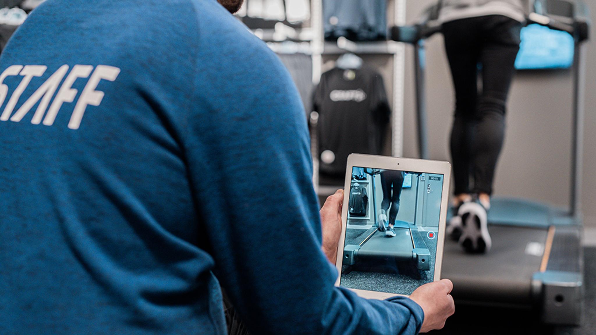a man is holding a tablet in front of a person on a treadmill .
