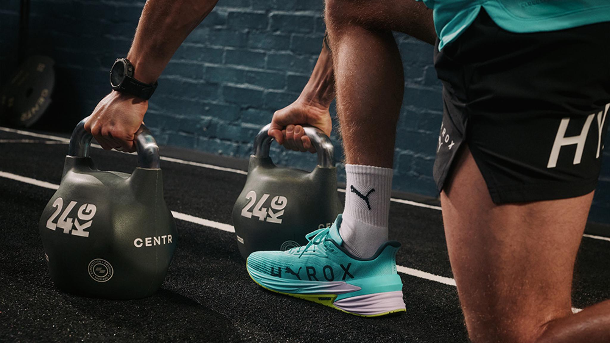 A person in workout gear holds two 24kg kettlebells in a gym.