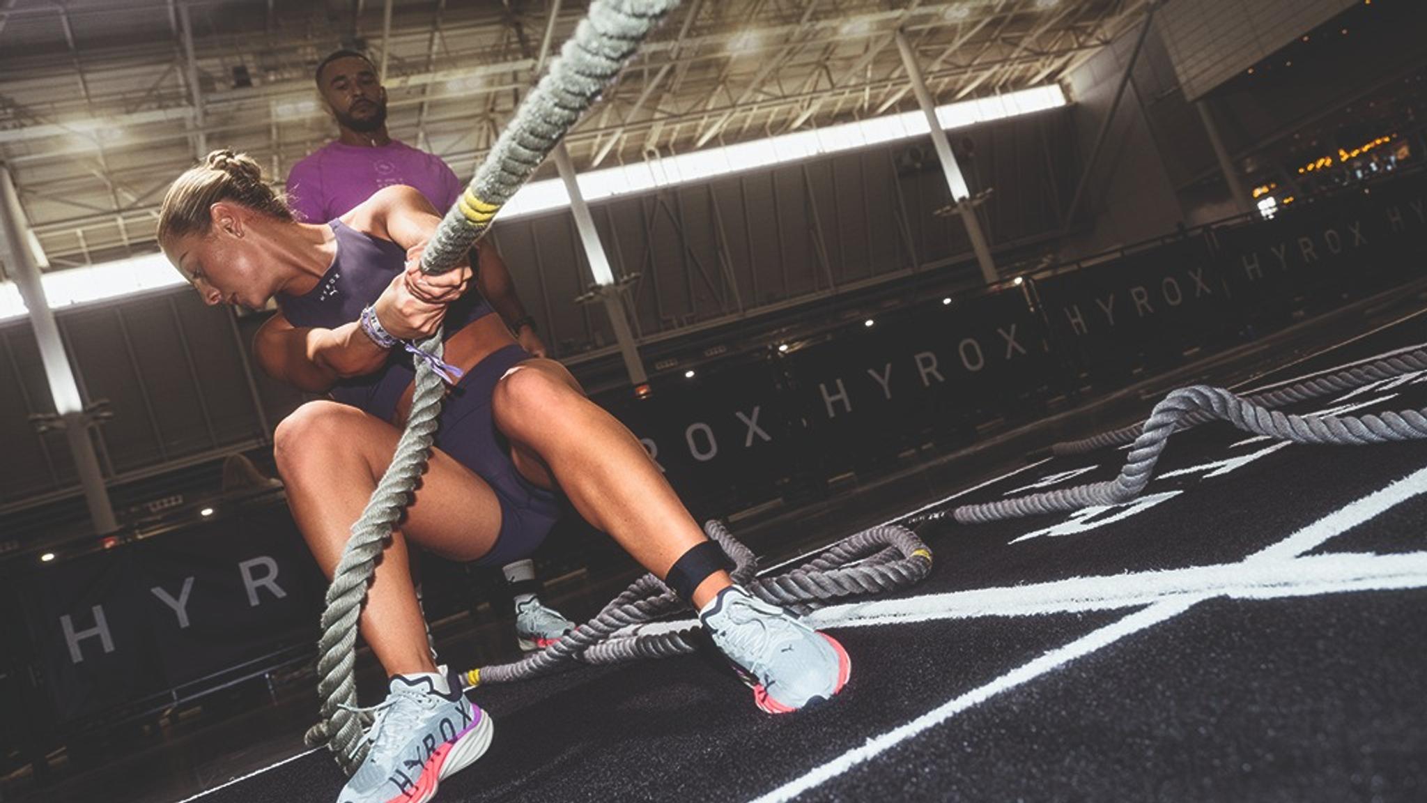 a woman is pulling a rope in a gym while a man watches .