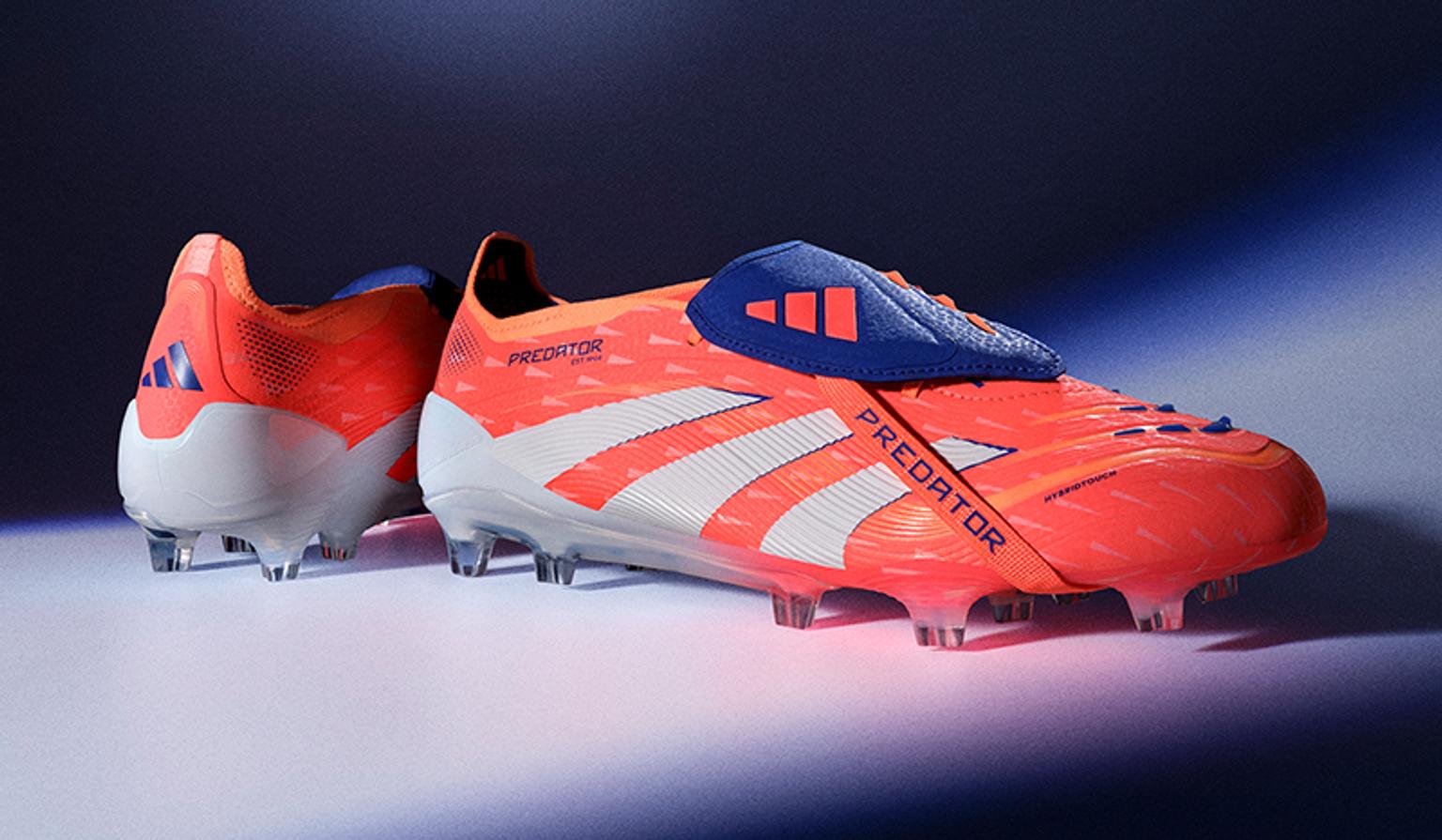 a pair of orange and white adidas predator soccer cleats are sitting on a table .