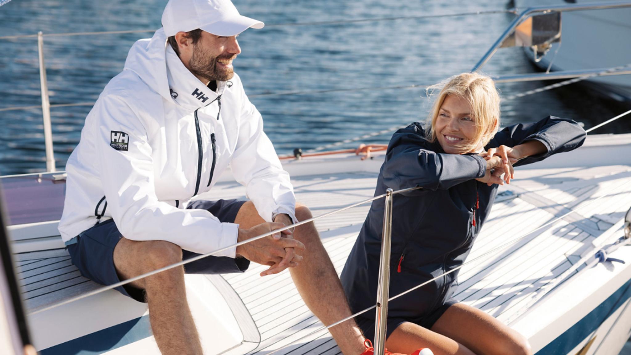 Man and woman in Helly Hansen sailing gear smiling on a sailboat.