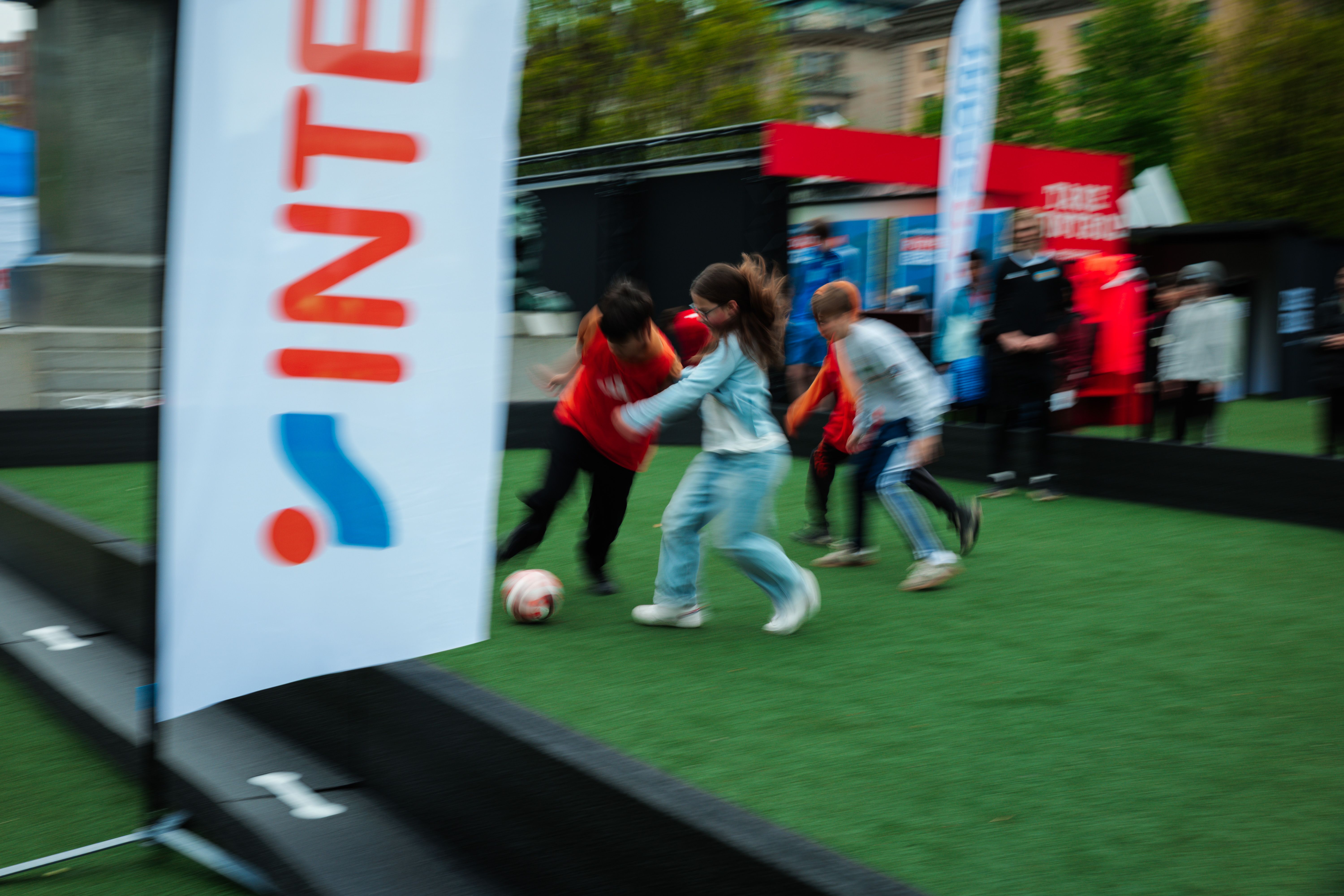 Children playing soccer on a green turf with motion blur, an Intersport banner visible.
