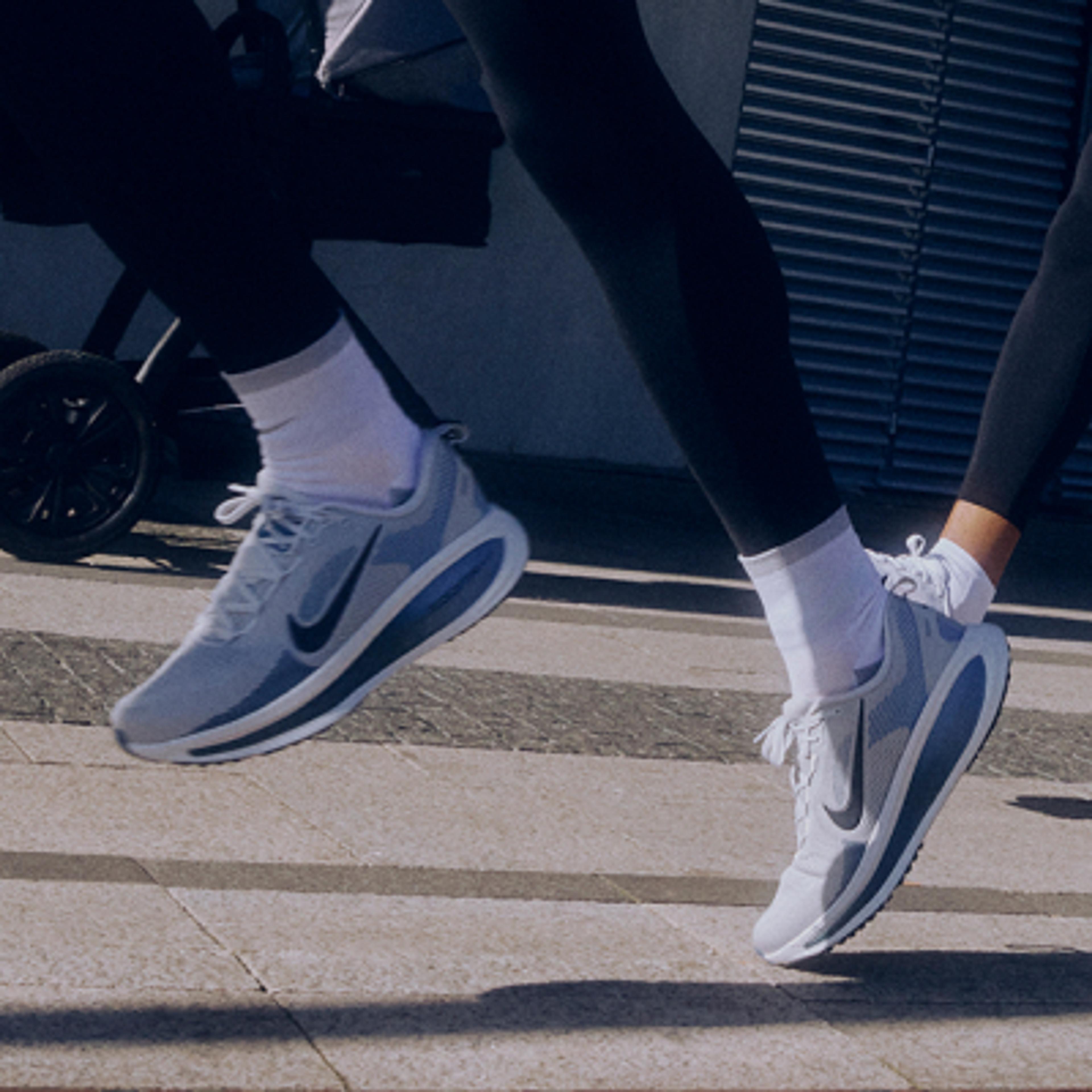 Two people running in grey Nike sneakers with blue accents on a paved surface.
