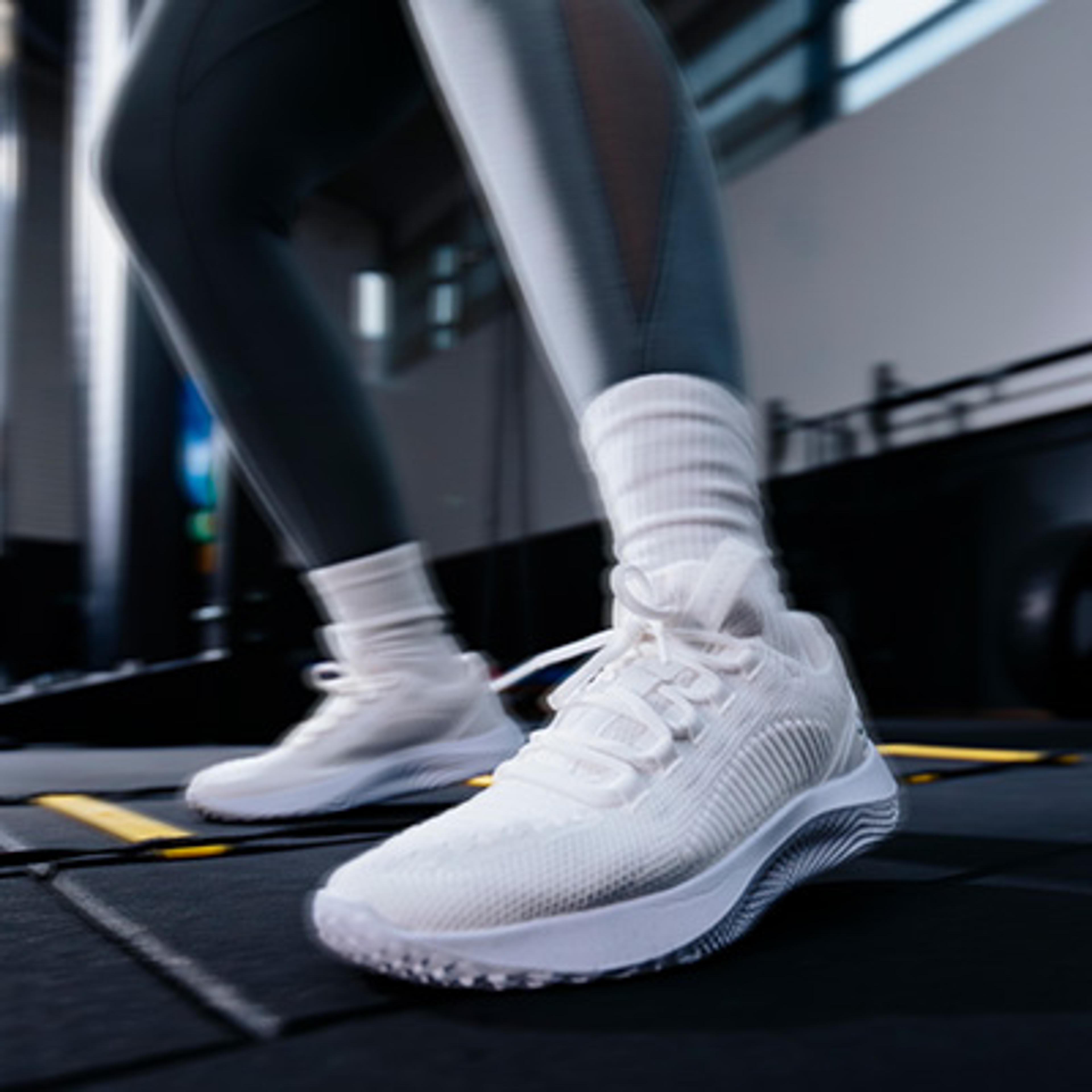 Close-up of a person's feet in white sneakers and dark leggings, in motion on a dark surface.