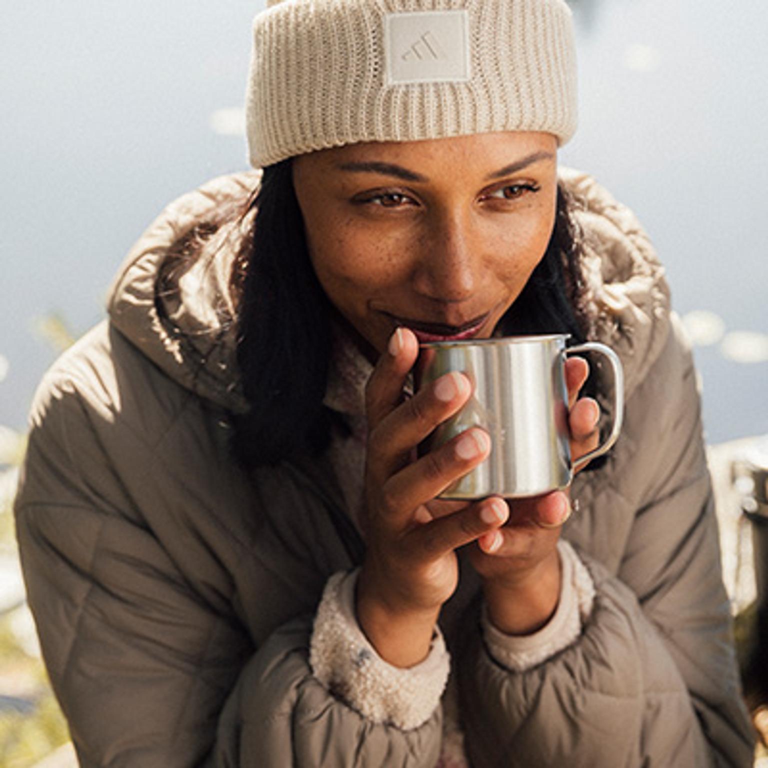 a woman is drinking from a stainless steel mug .